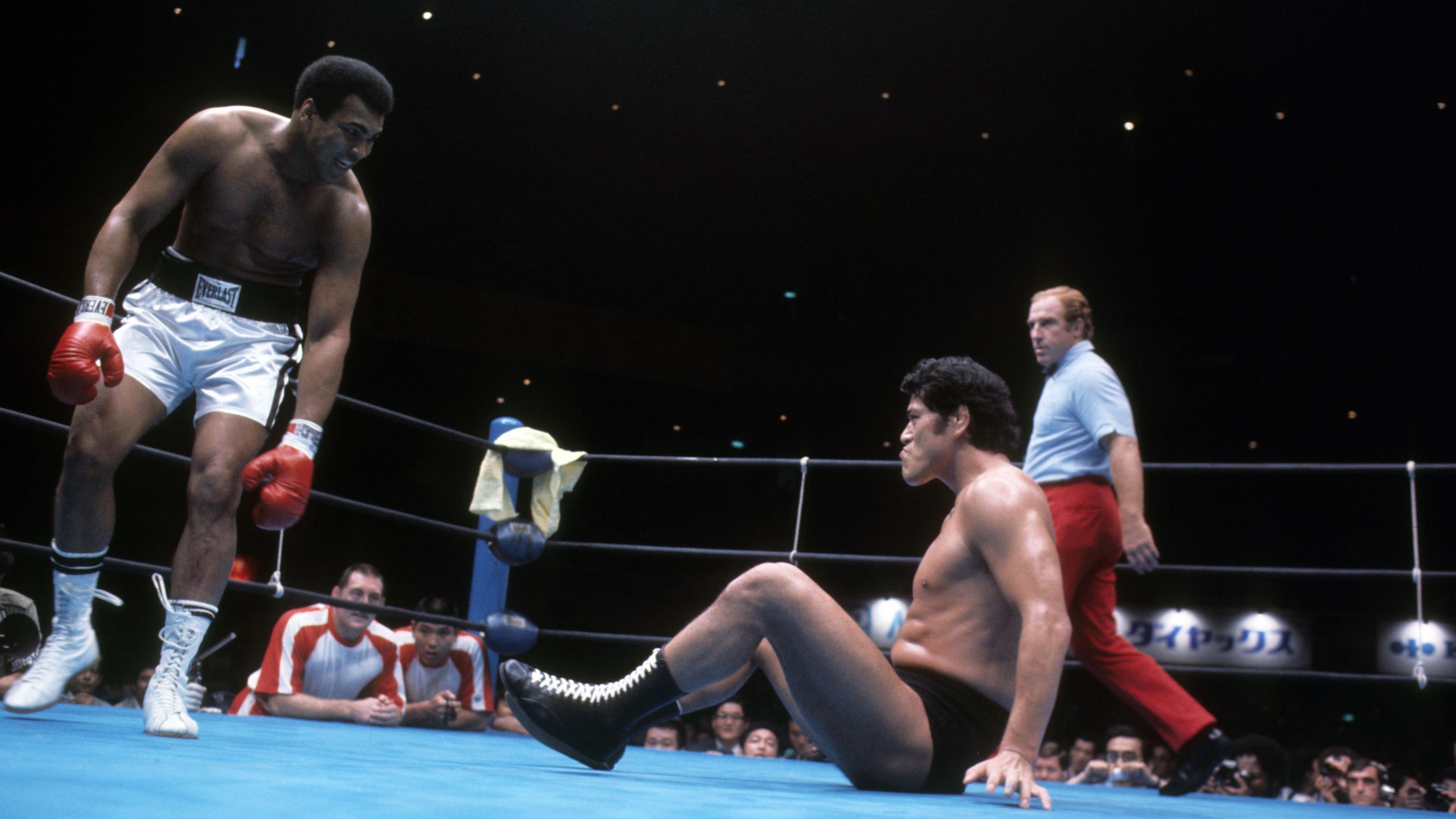 Ali looks down at Inoki who is on the floor as the referee looks on