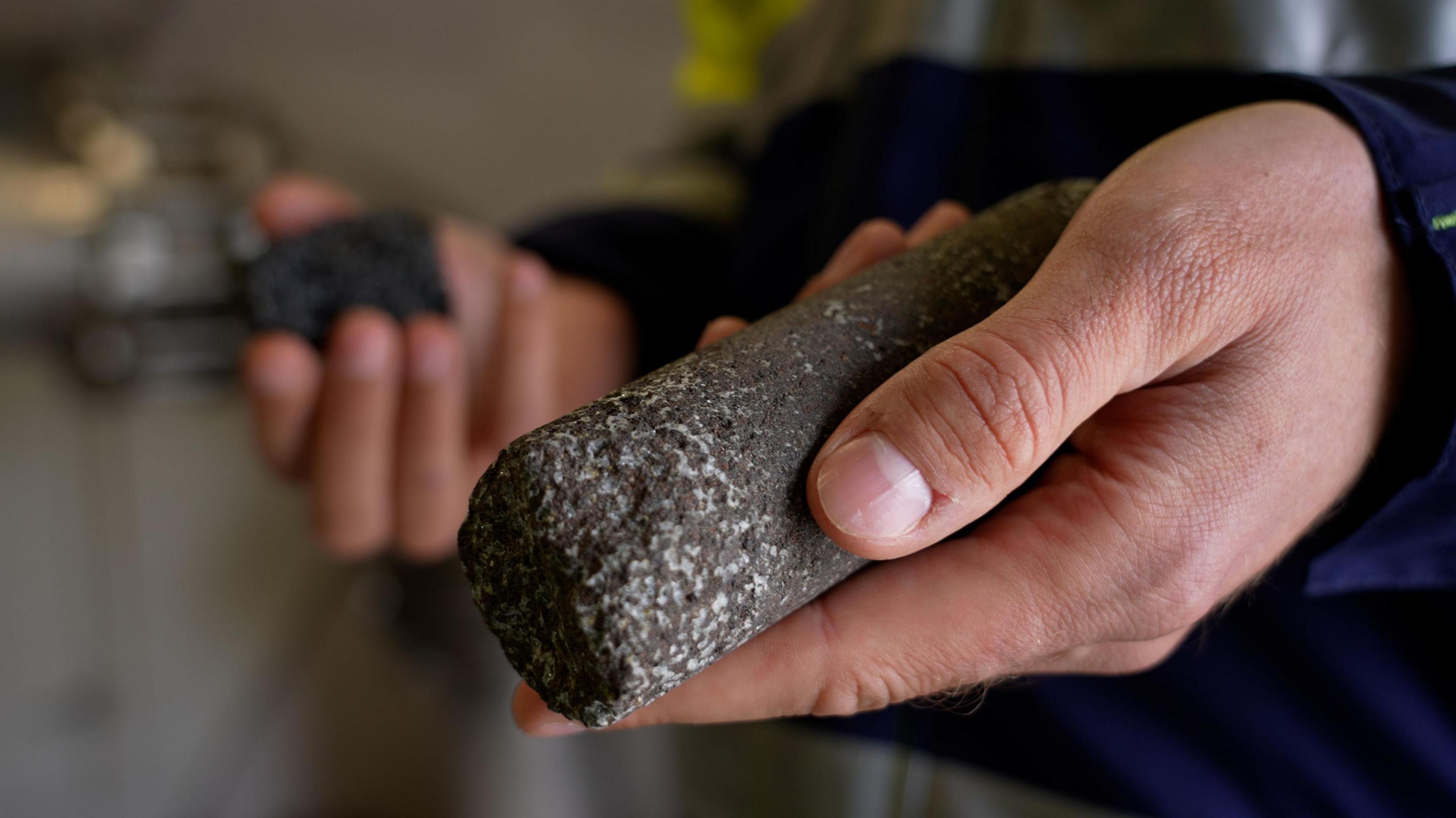 A man holds a cylindrical piece of black Icelandic bedrock with captured white carbon