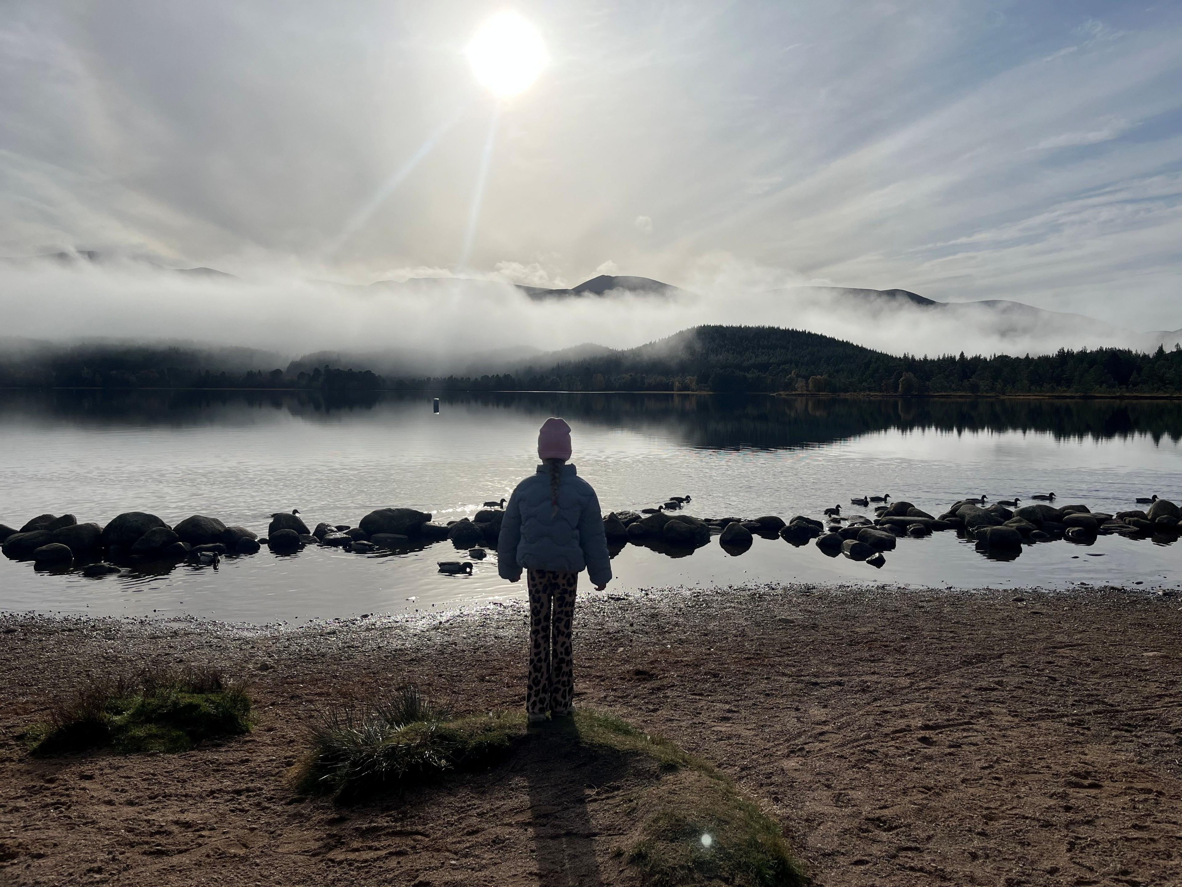 A young girl standing on a beach, looking out to the sea in front of her