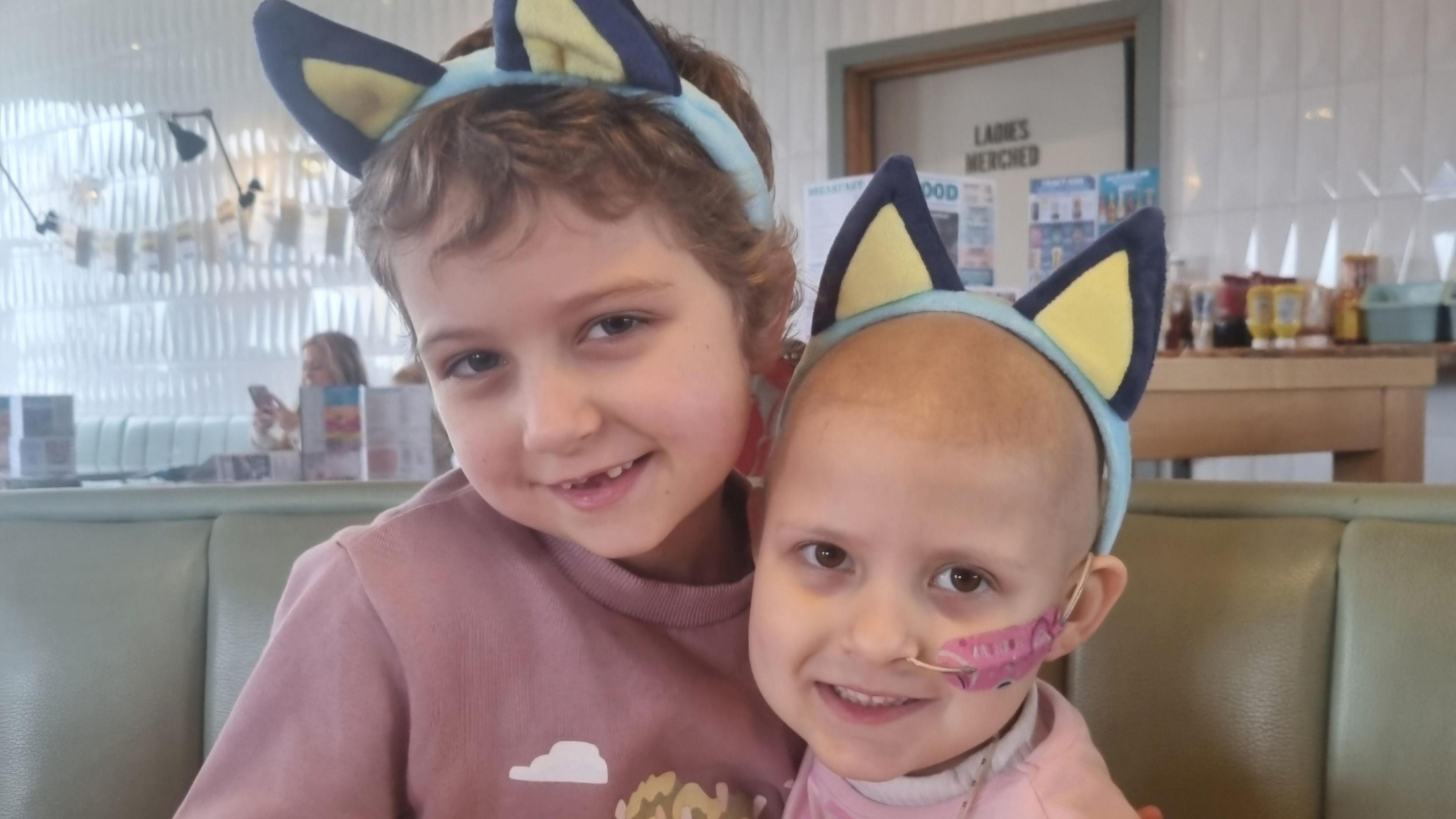 Betsy (left) and Lacie. Both are wearing headbands with animal ears. Lacie has lost her hair and has a tube up her nose. 