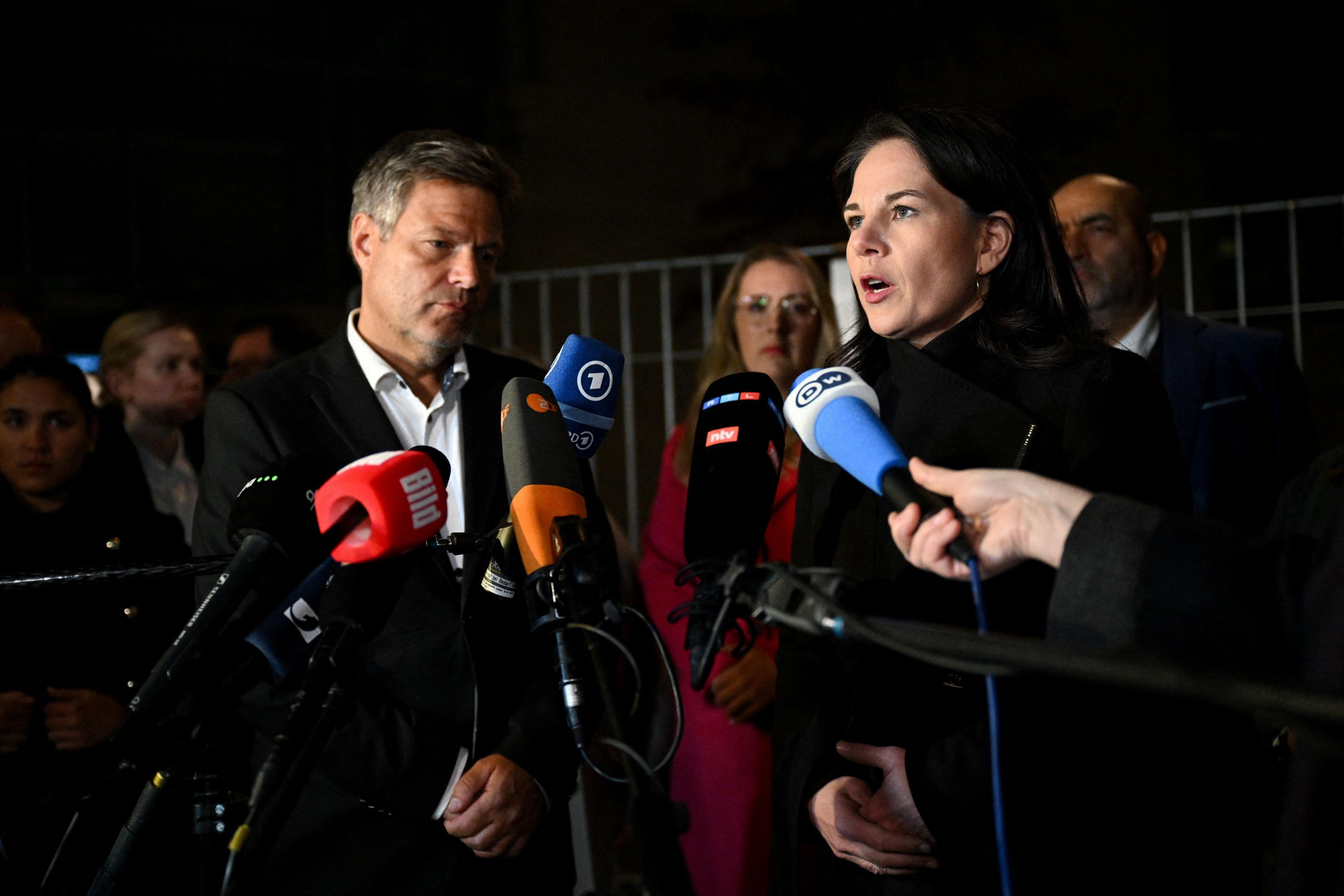 Economy Minister Robert Habeck wearing a suit and shirt and Foreign Minister Annalena Baerbock wearing a black coat stand in front of microphones to speak to the press.