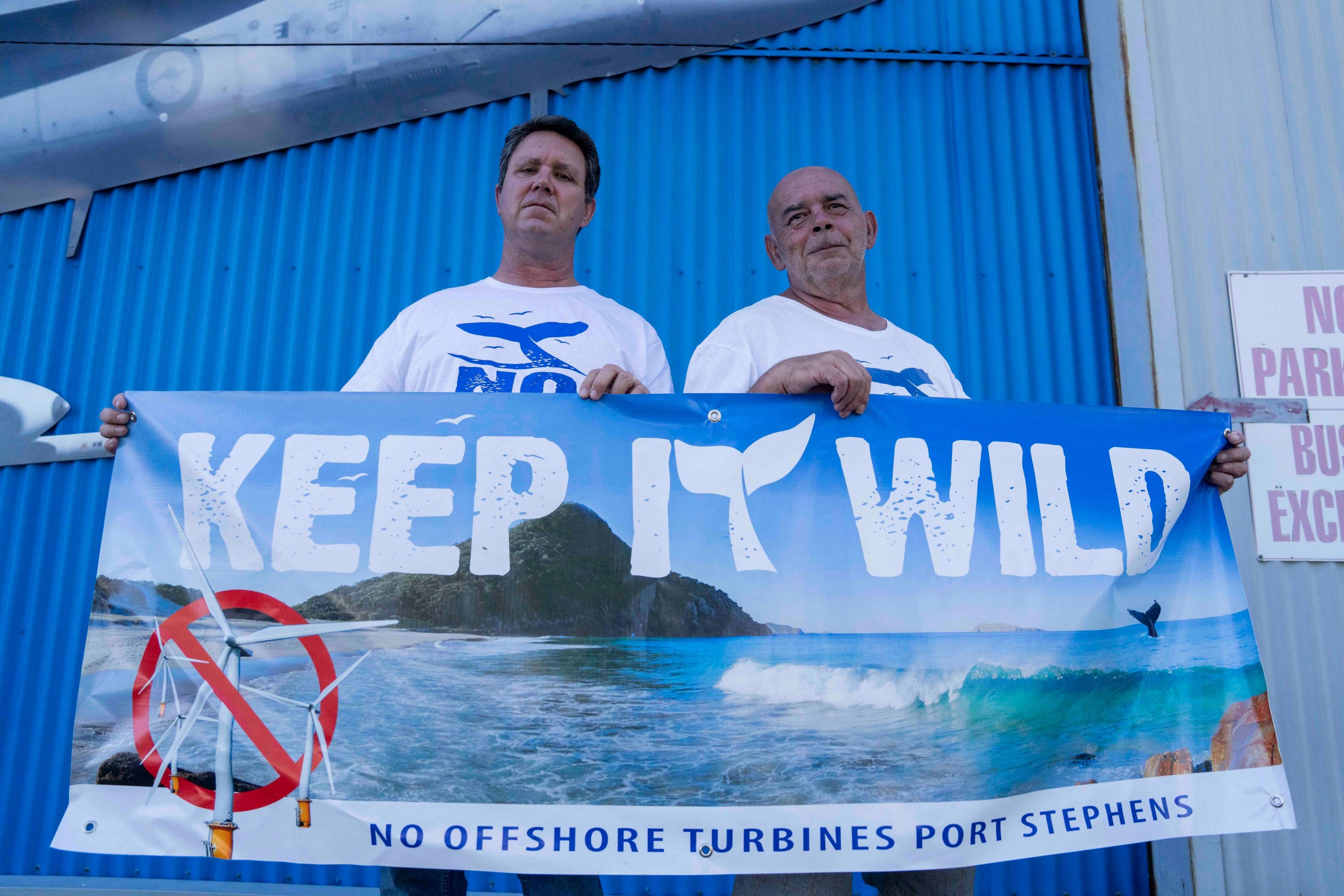 Ben Abbott and colleague John Hamilton (right) hold up a banner protesting plans to build offshore wind turbines near Port Stephens