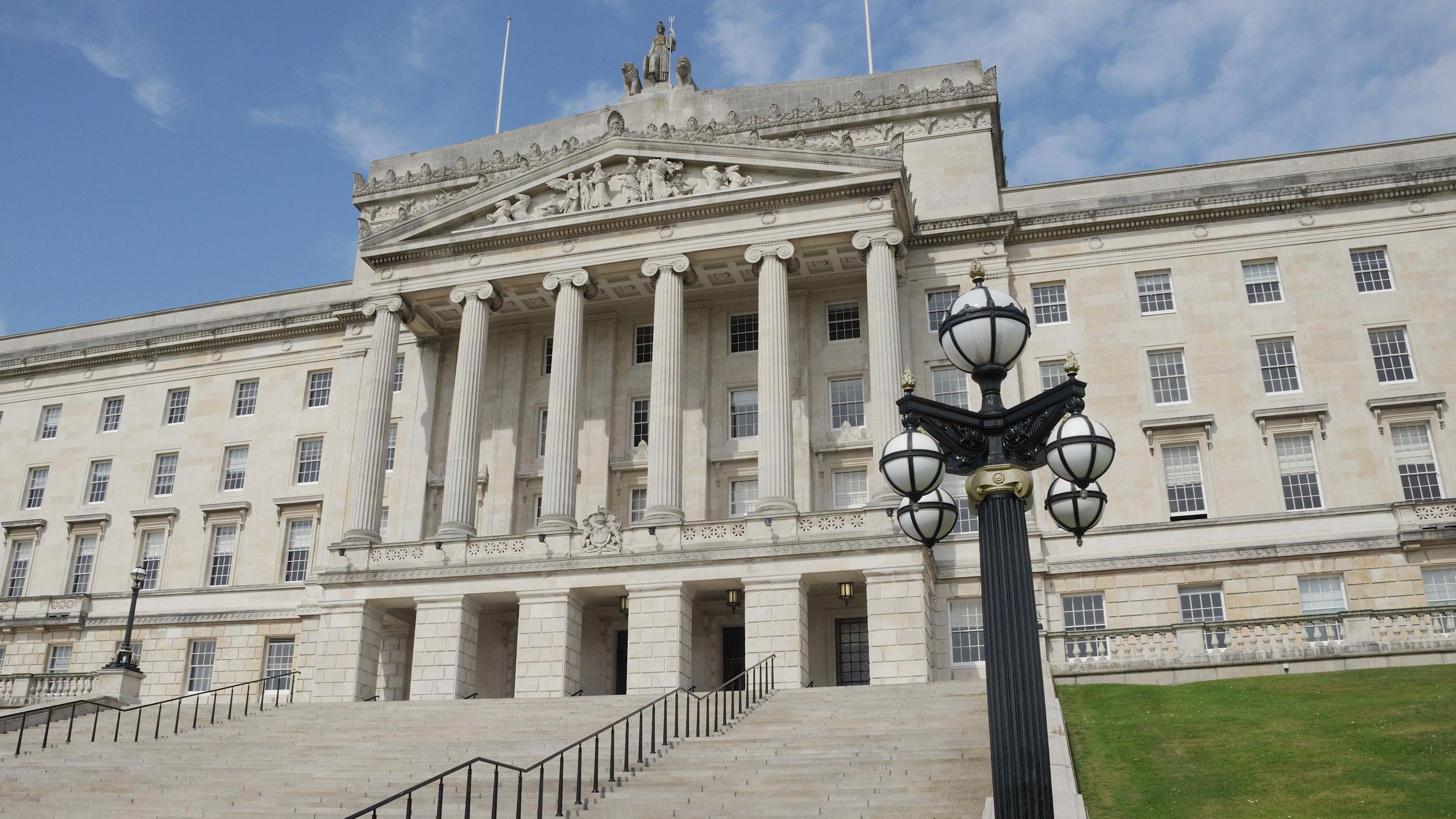 Parliament building at Stormont is a large white building with columns. There are steps leading up to it with grass on both sides.