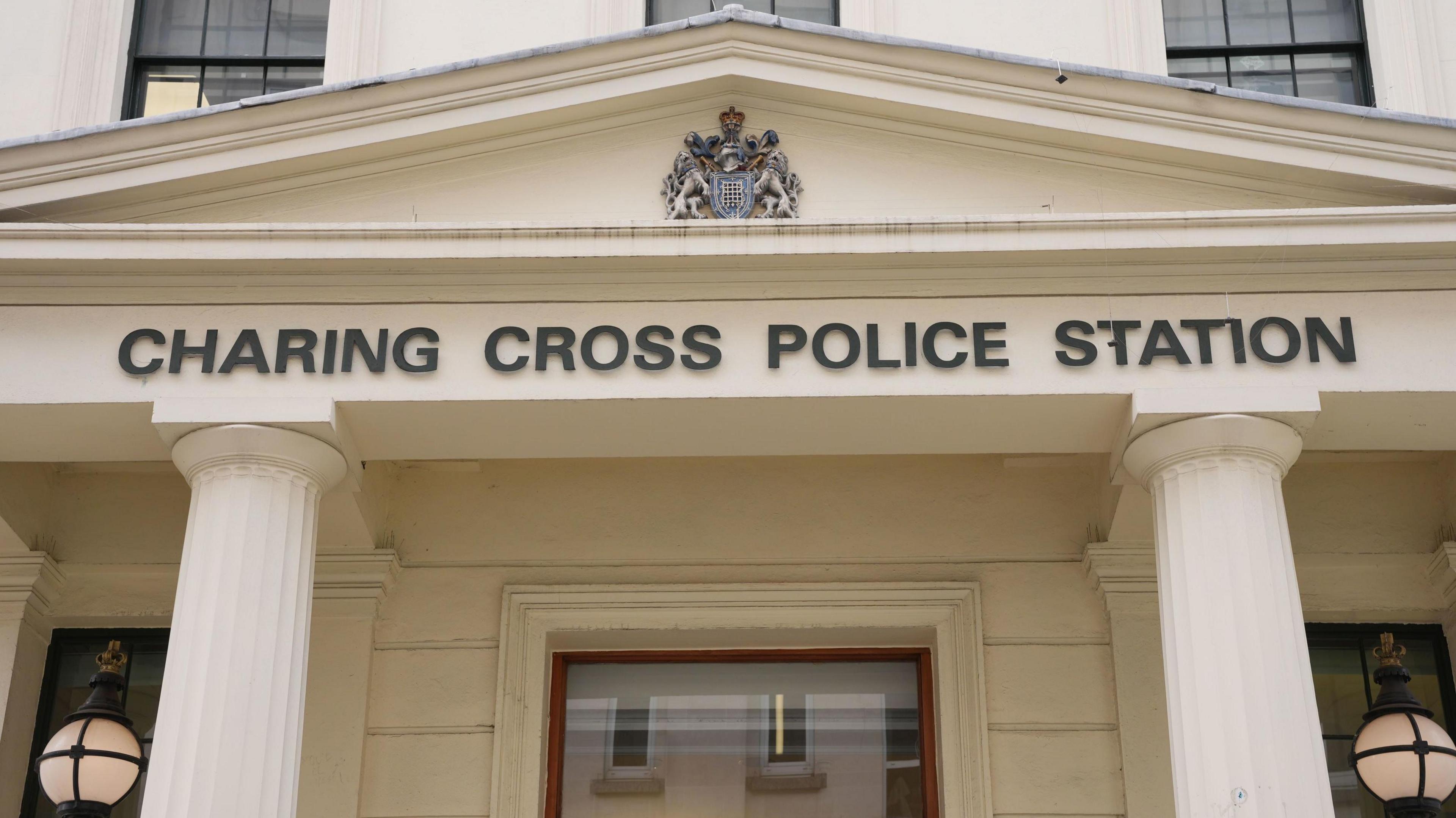 Black Charing Cross police station sign below a coat of arms and two white pillars and lights