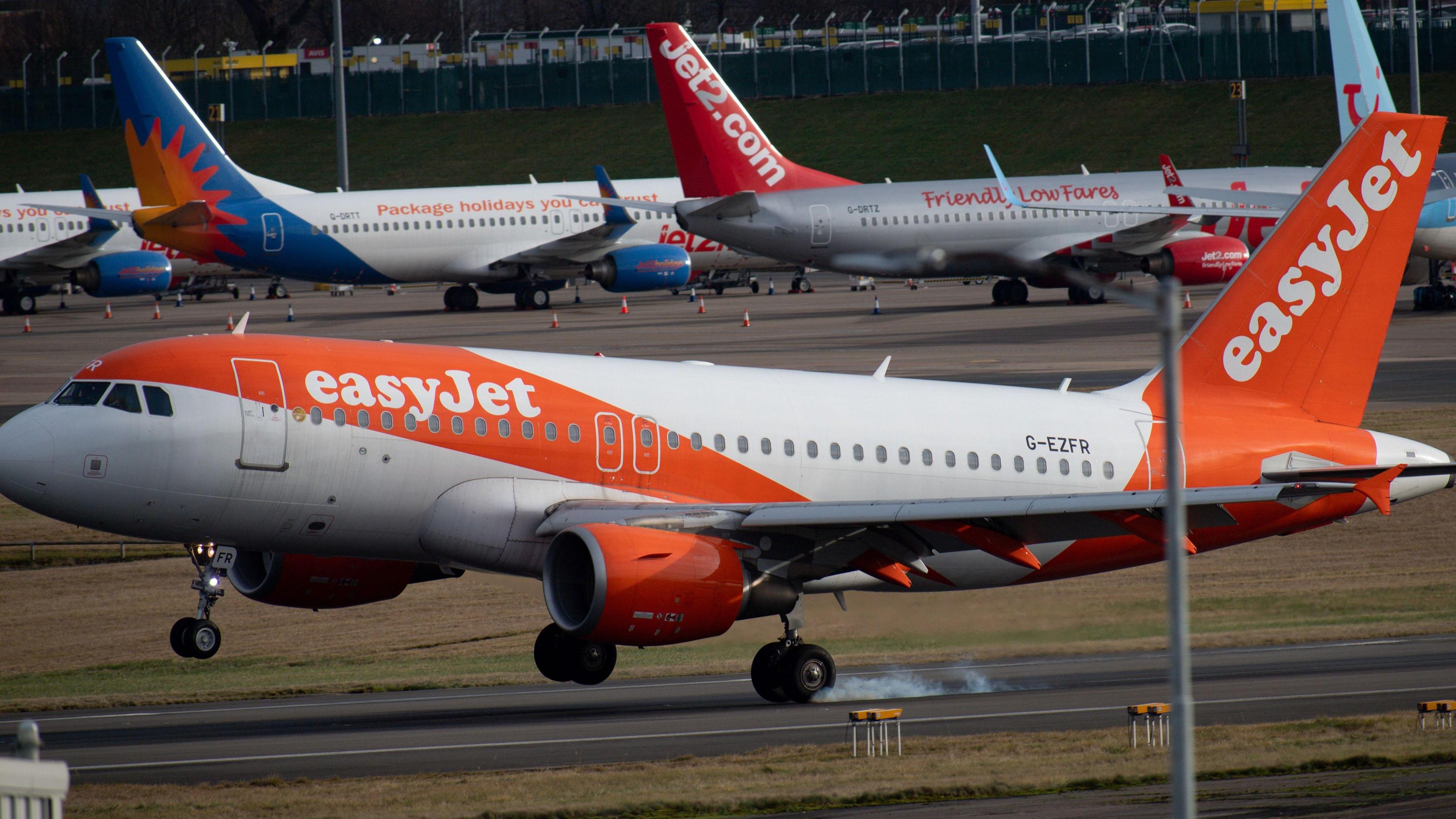 An easyJet plane lands on a runway in the foreground with planes lined up in the background.