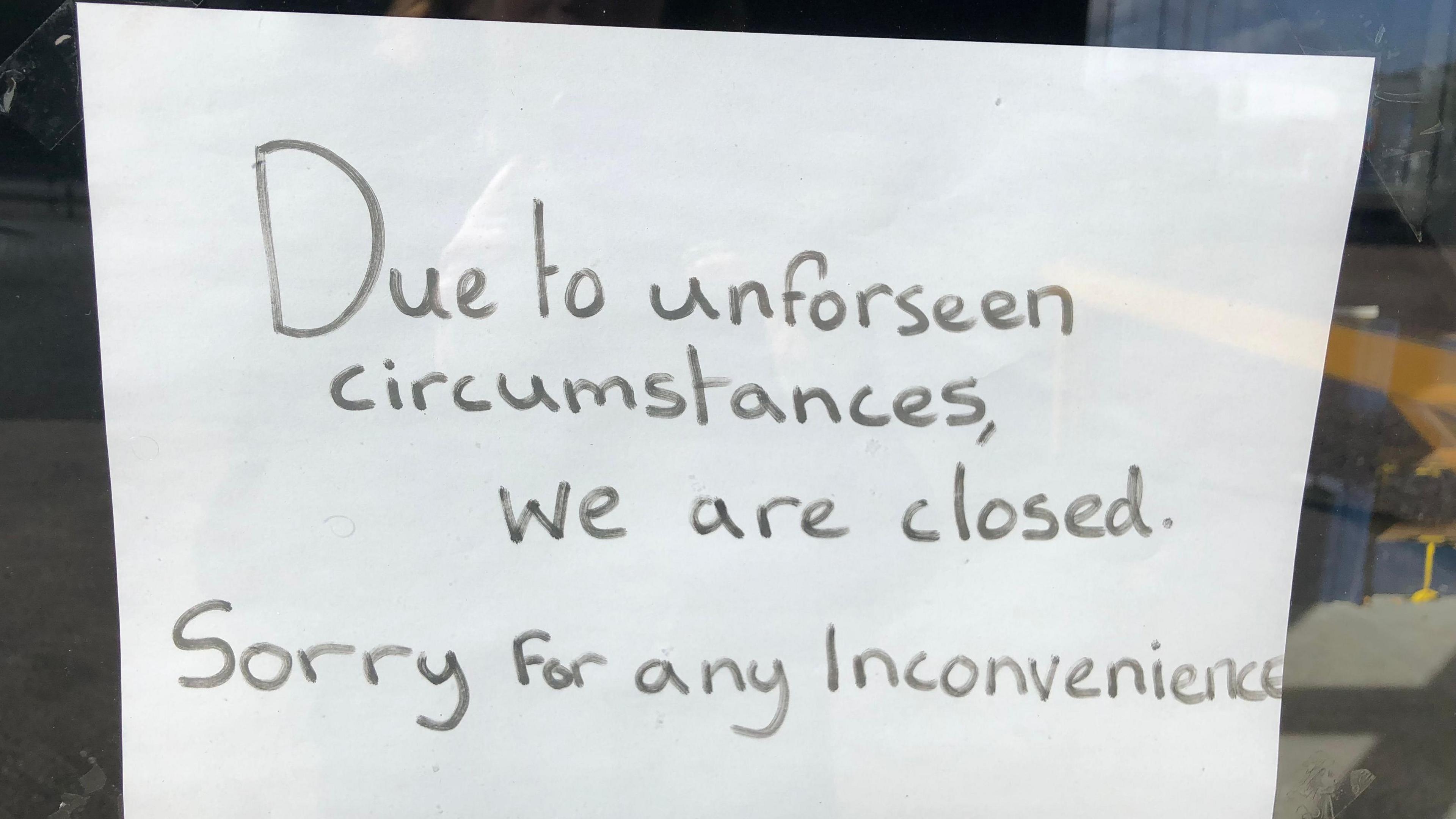 A sign posted in a window written in black marker which says "due to unforeseen circumstances, we are closed. Sorry for any inconvenience". 