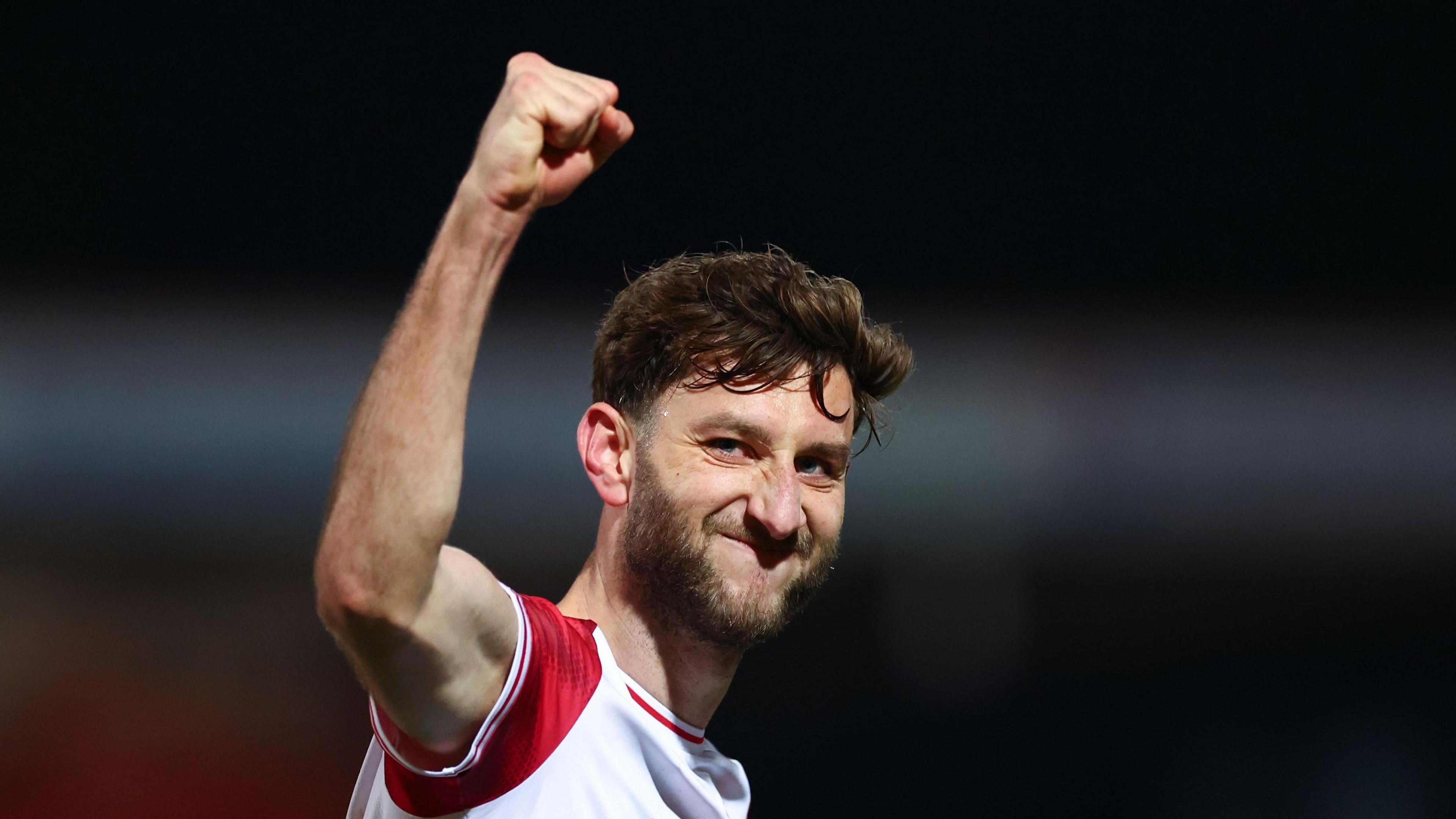 Charlie Goode, in action for Stevenage, celebrates by raising a clenched fist towards the supporters.