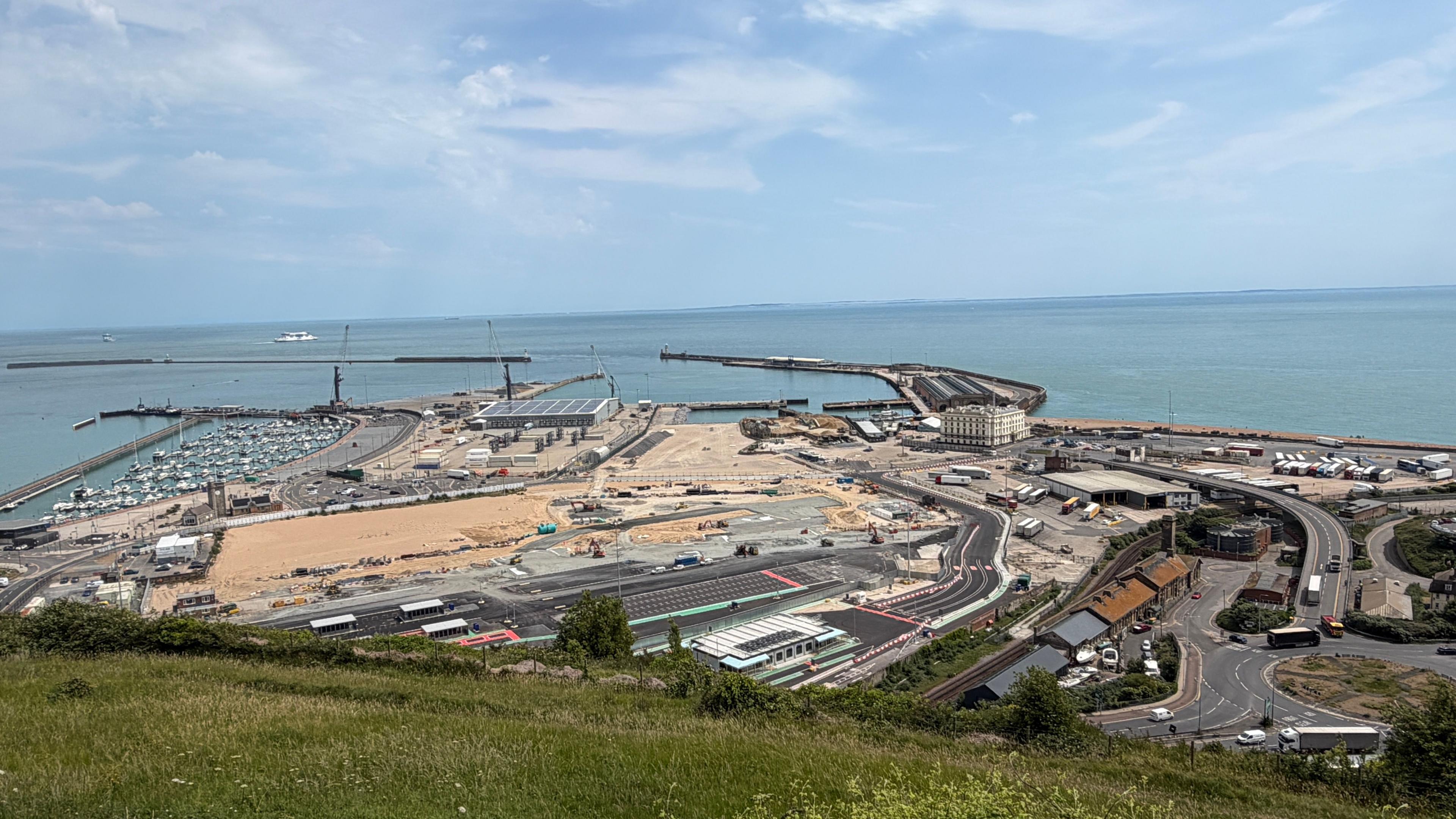 An aerial view of dover showing a road network, a large area of new tarmac and sand and land leading down to the sea with a marina