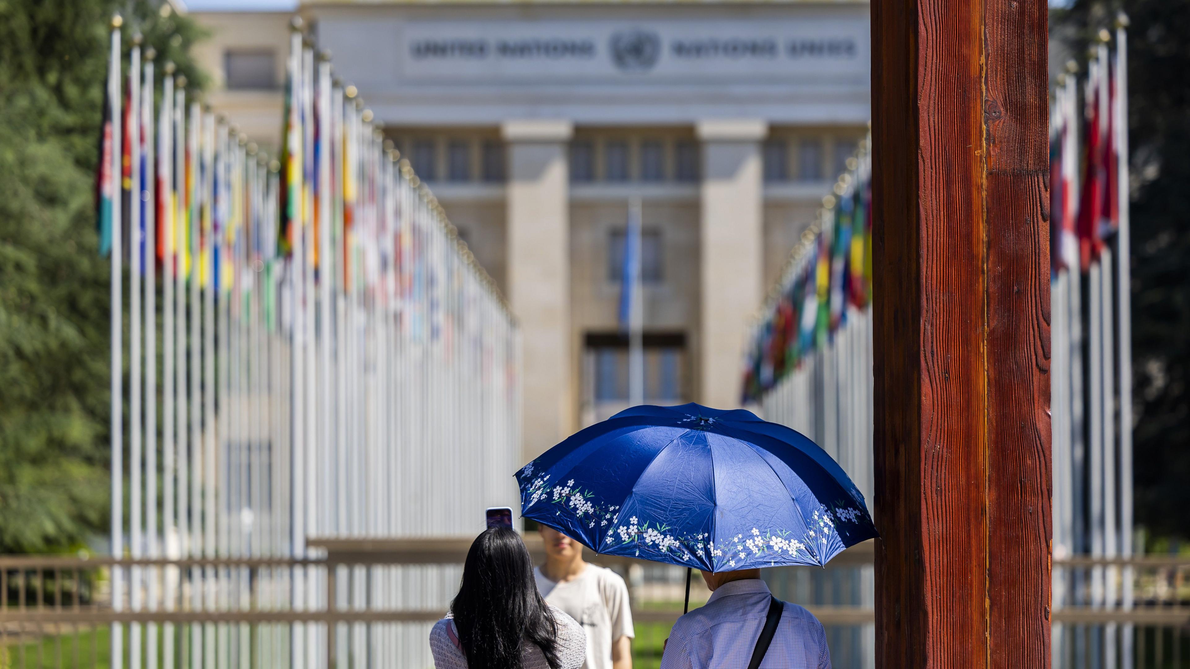 A tourist takes photos as another holds an umbrella for sun protection at Place des Nations in front of the European headquarters of the United Nations during a heatwave alert in Geneva, Switzerland