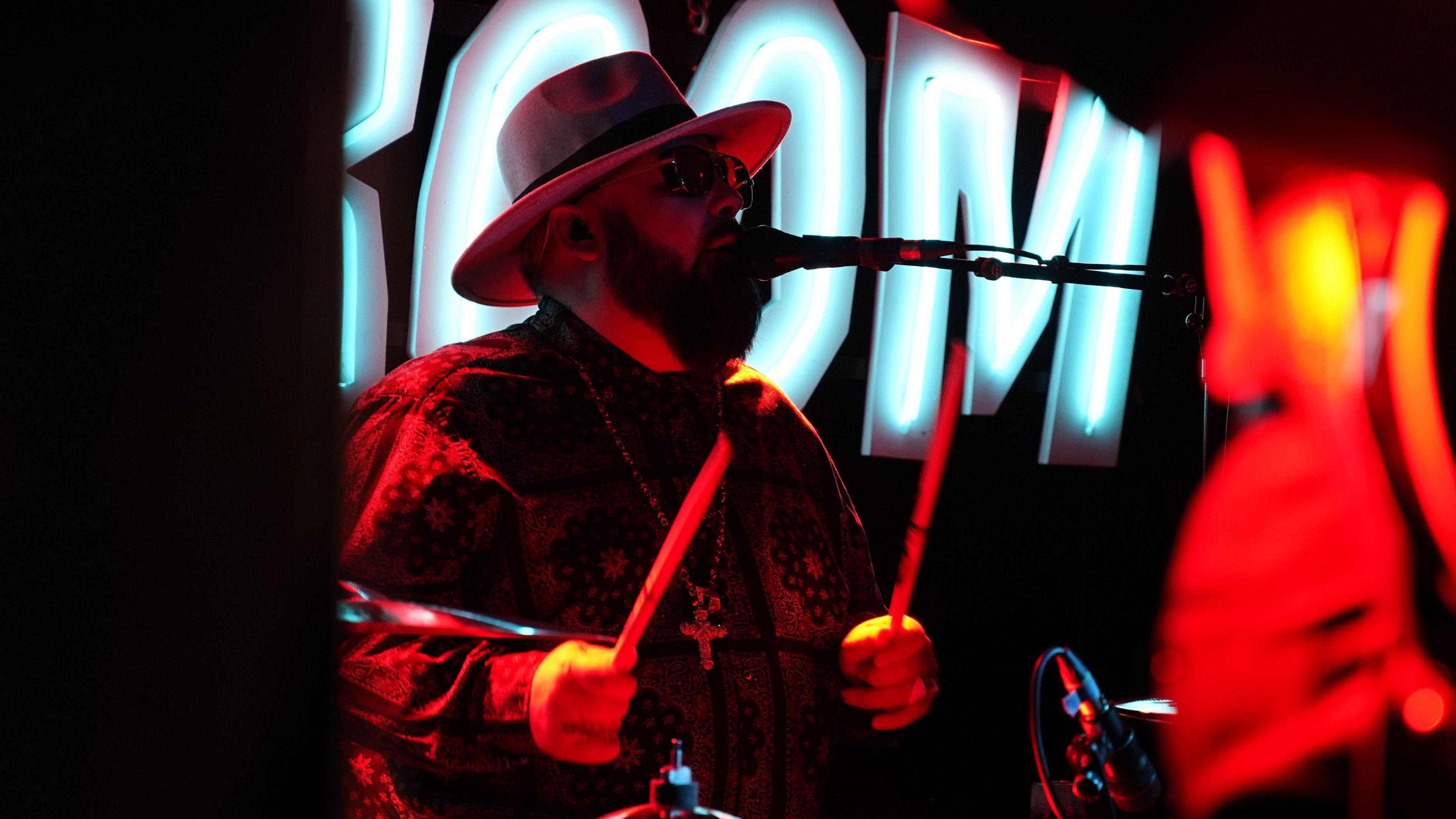 A drummer pictured singing in dim light.