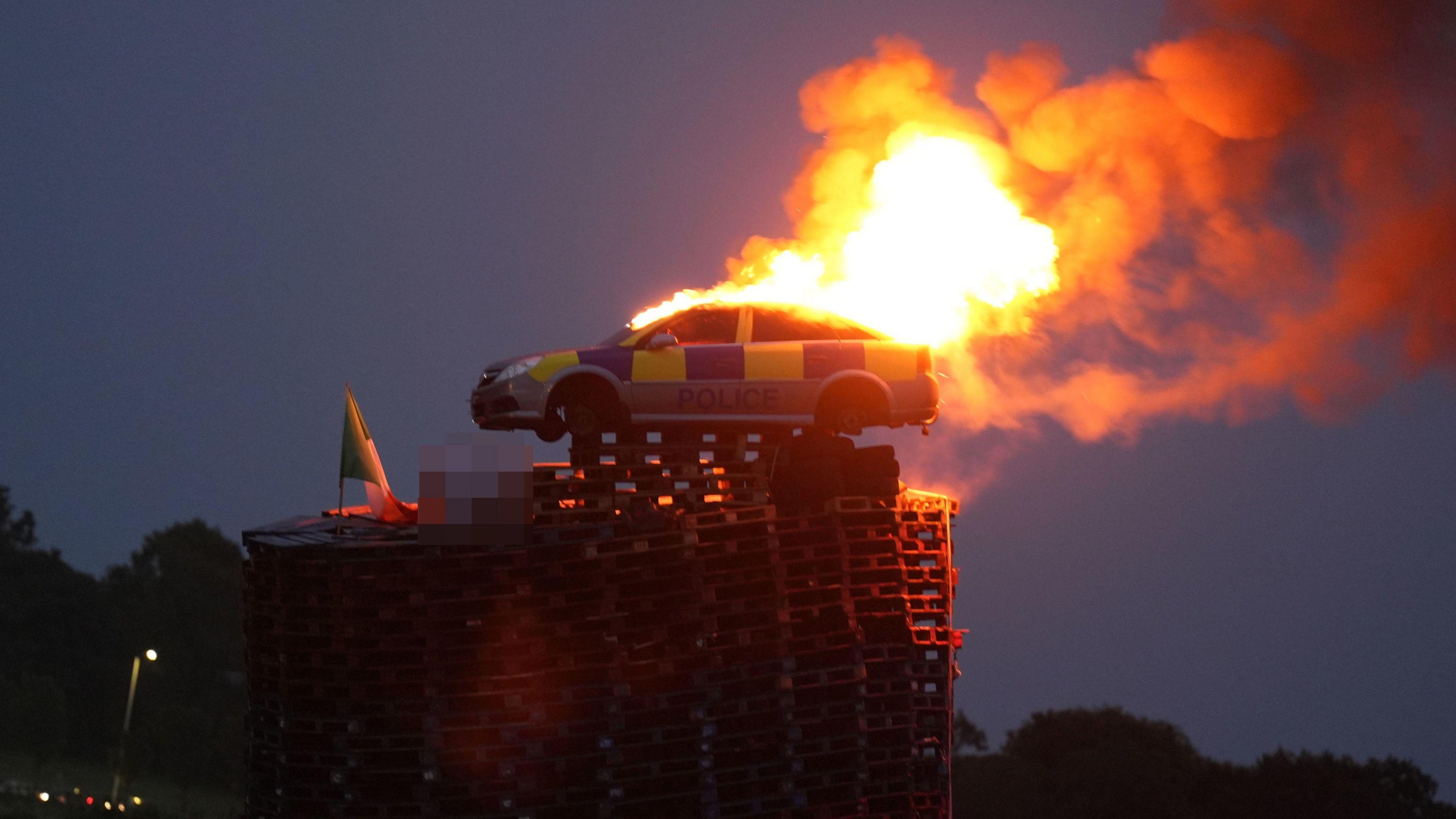 Burning mock police car on top of bonfire made from pallets