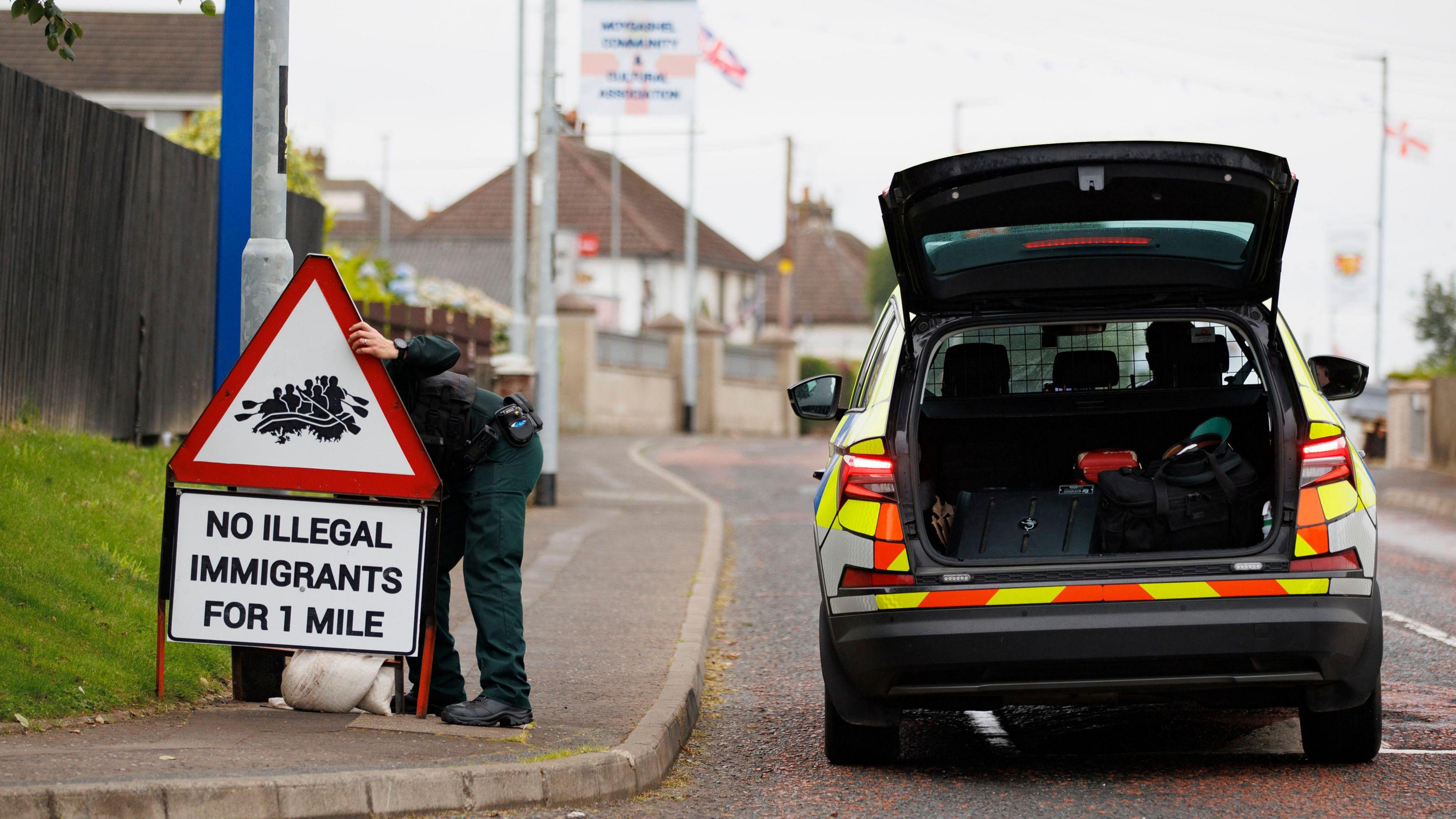 Red sign saying "NO ILLEGAL IMMIGRANTS FOR 1 MILE" being removed by a police officer in uniform