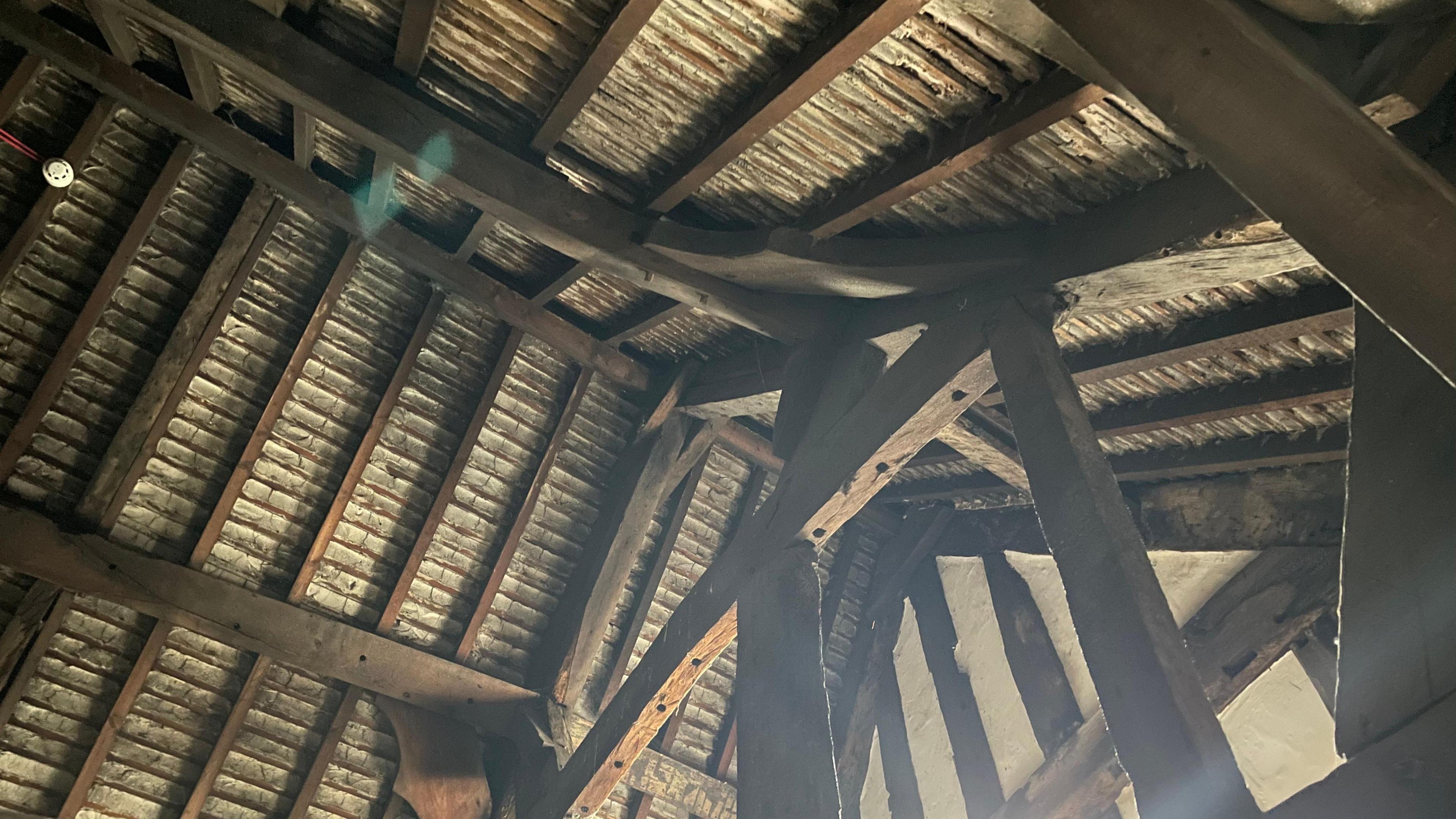 The inside roof of an old mansion building. It is wooden with large dark wood beams, as well as wooden supports.