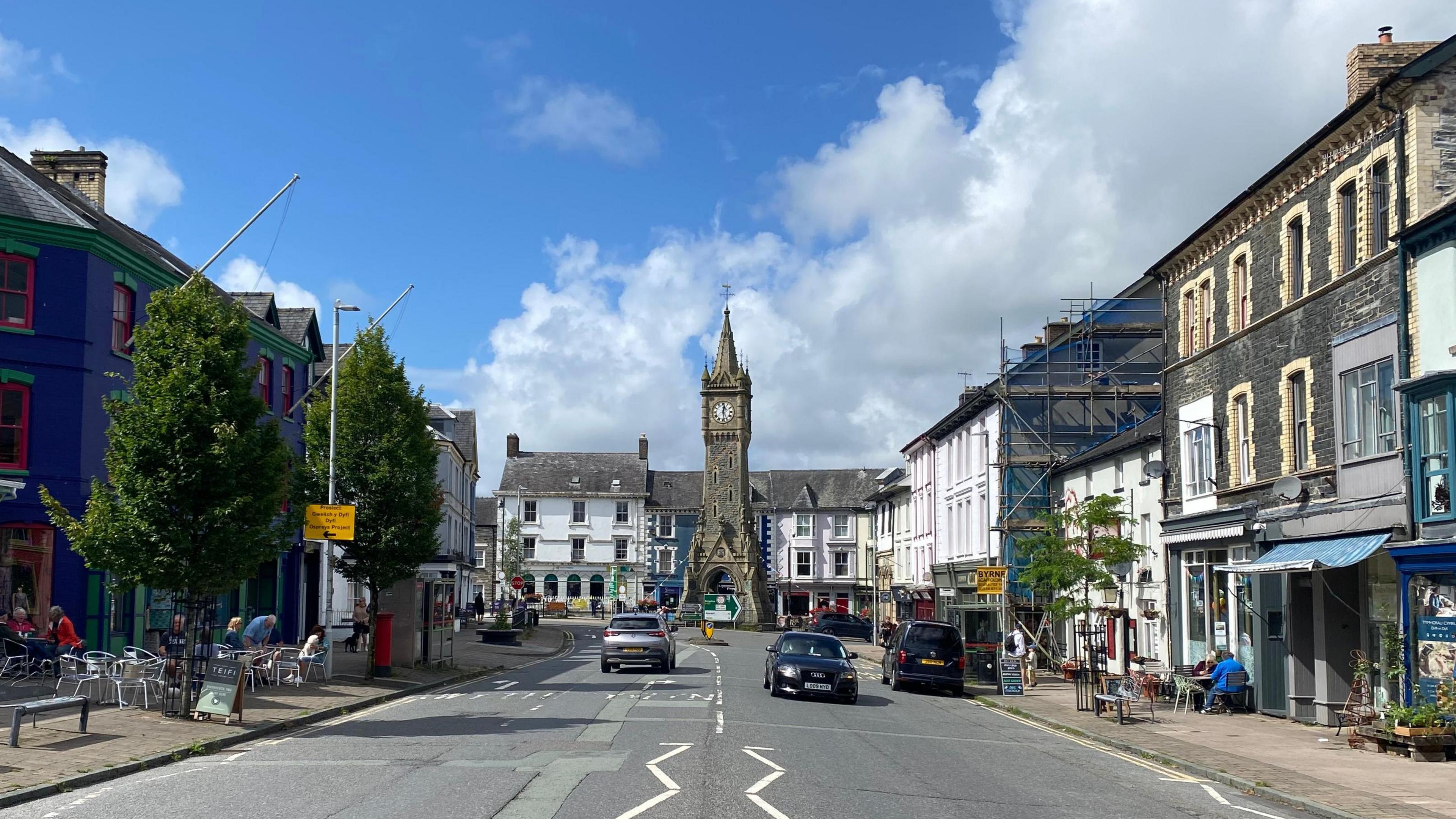 Canol tref Machynlleth ar ddiwrnod braf gyda'r cloc yn y cefndir