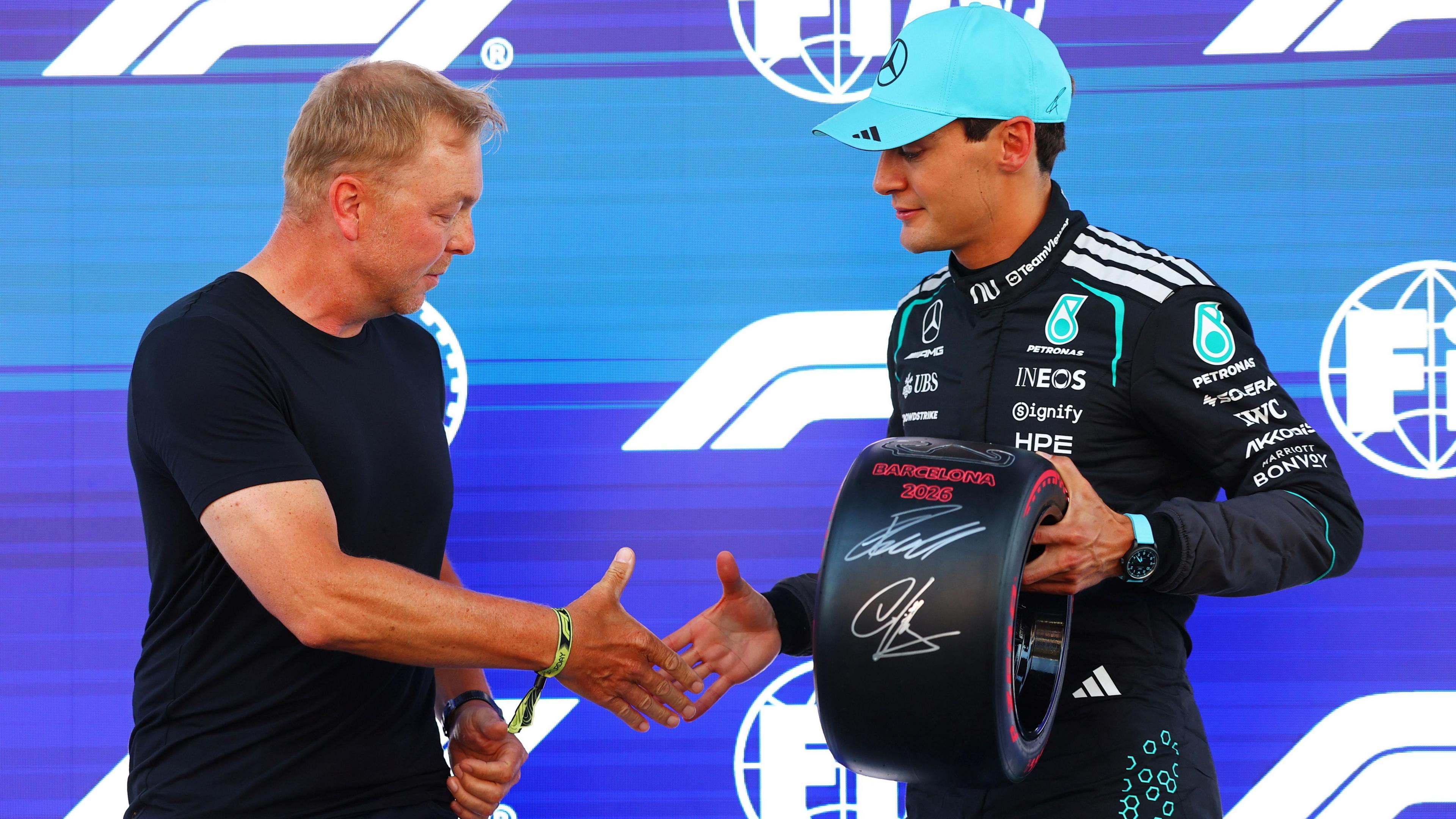 Sir Chris Hoy and George Russell shake hands after the Olympic champion cyclist had presented the Mercedes driver with the pole position award in Barcelona