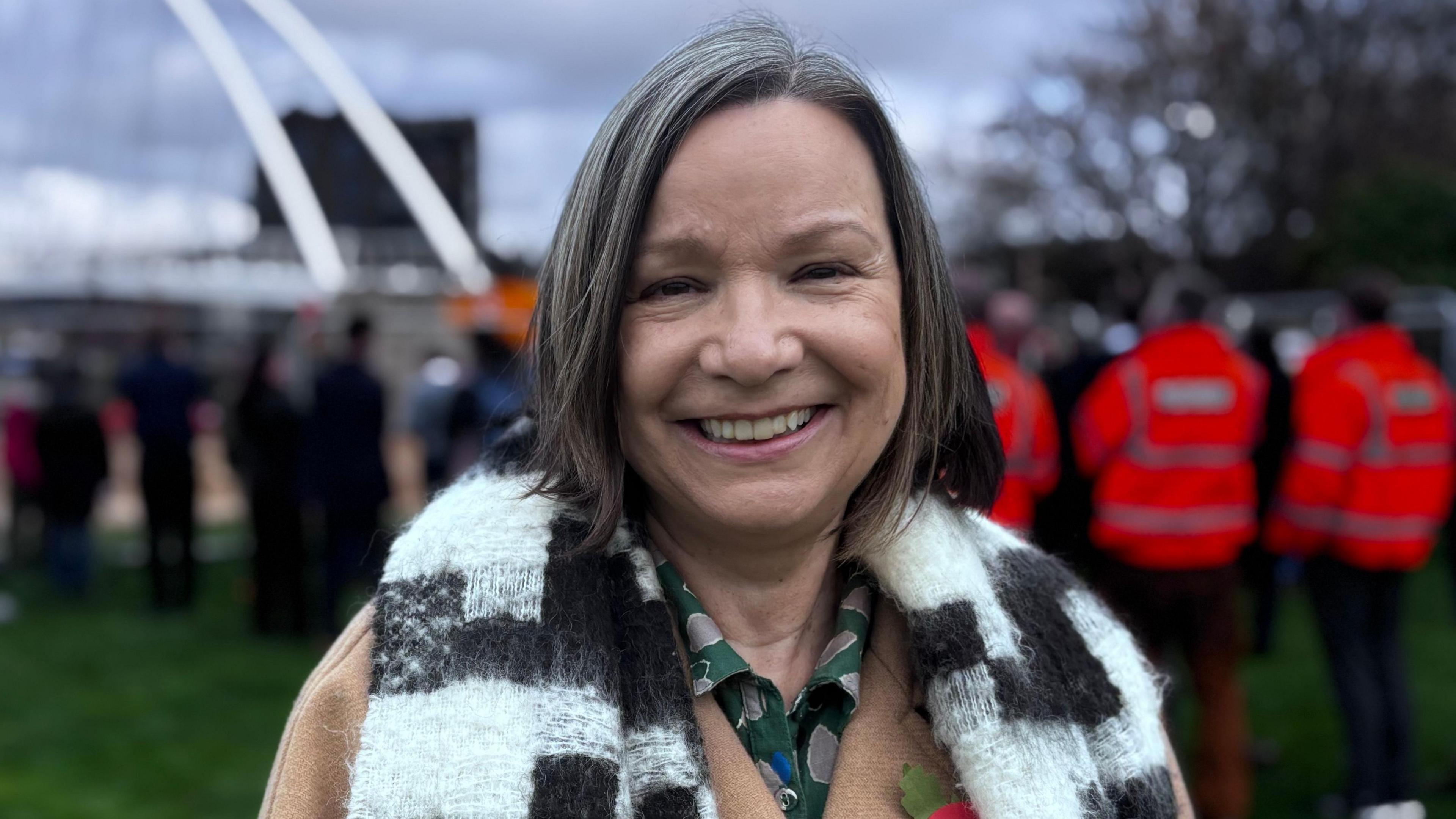 Councillor Linda Woodings at the installation of the bridge. Linda is a middle-aged White woman with short straight, greying her. She is wearing a camel coat with a black and white woolly scarf