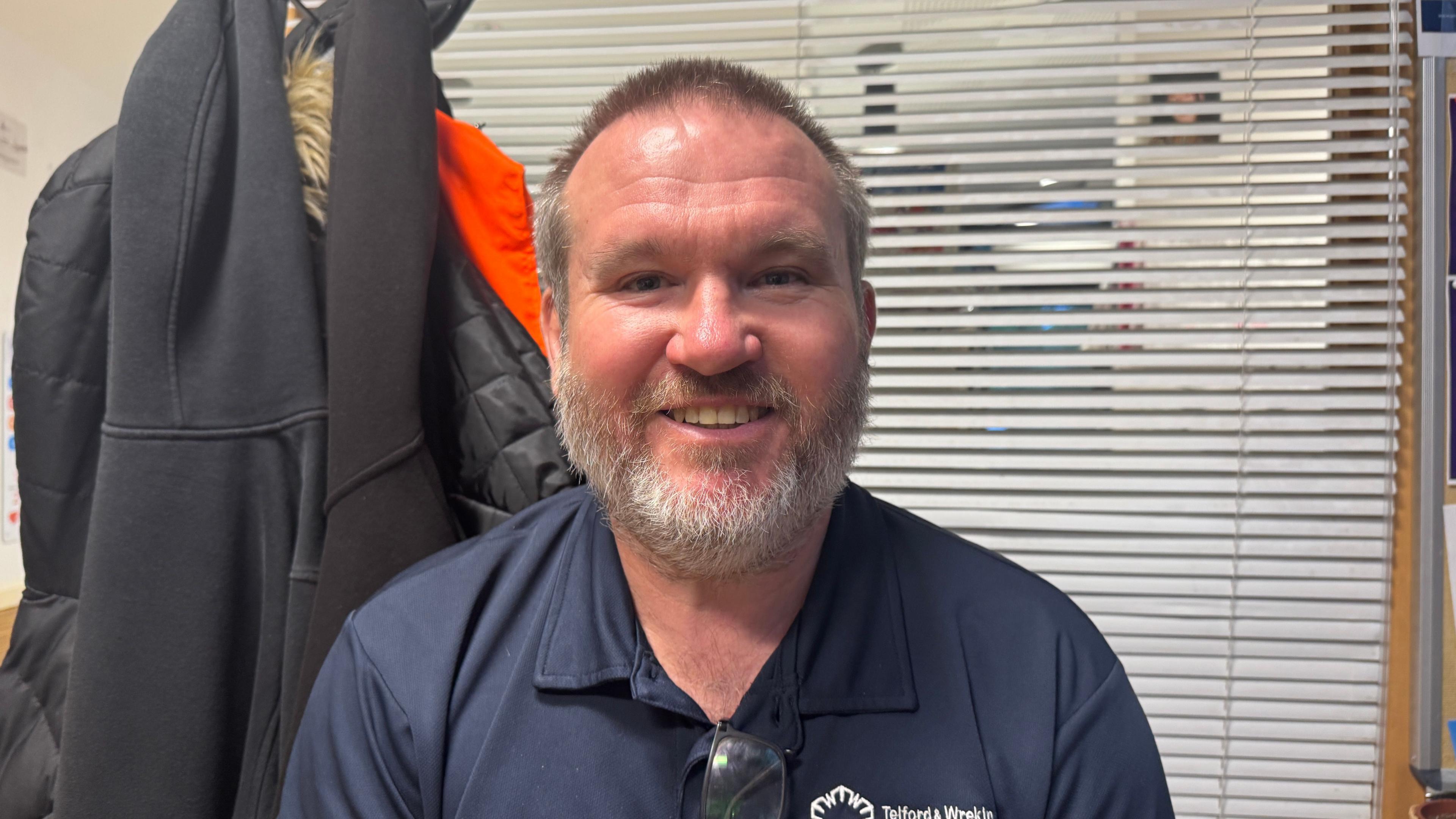 A man with short brown hair and grey and brown facial hair. He is wearing a navy T-shirt with the words "Telford and Wrekin Council" in white writing on the breast