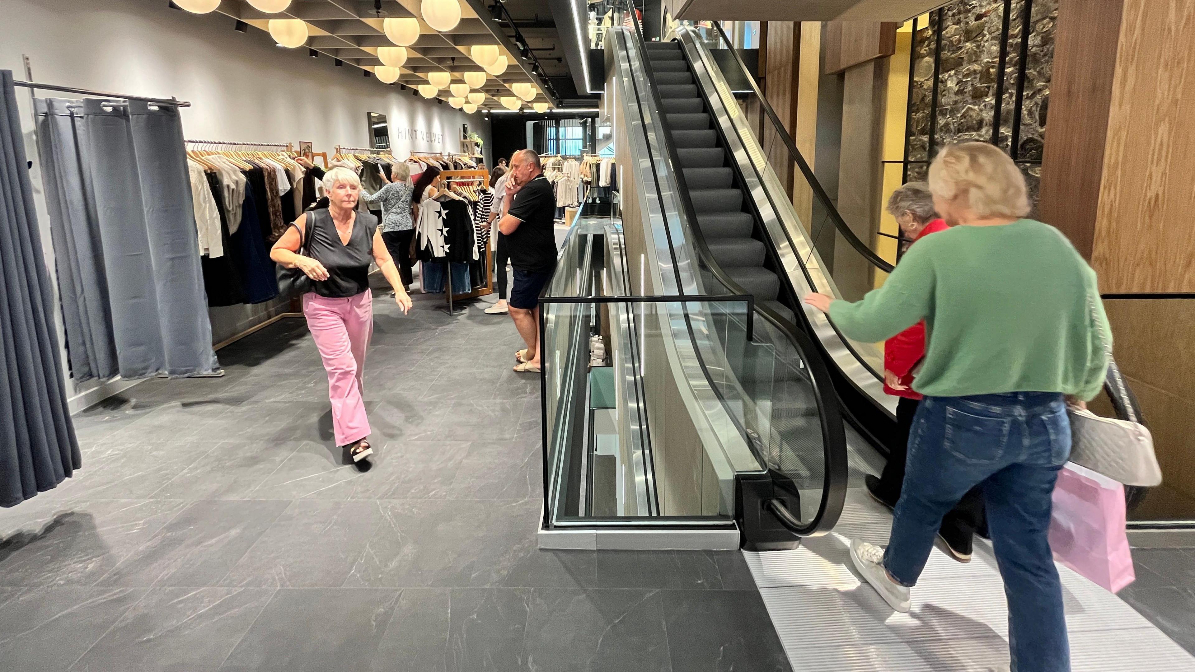 Customers shop for clothes and got up the escalator in a modern shop.
