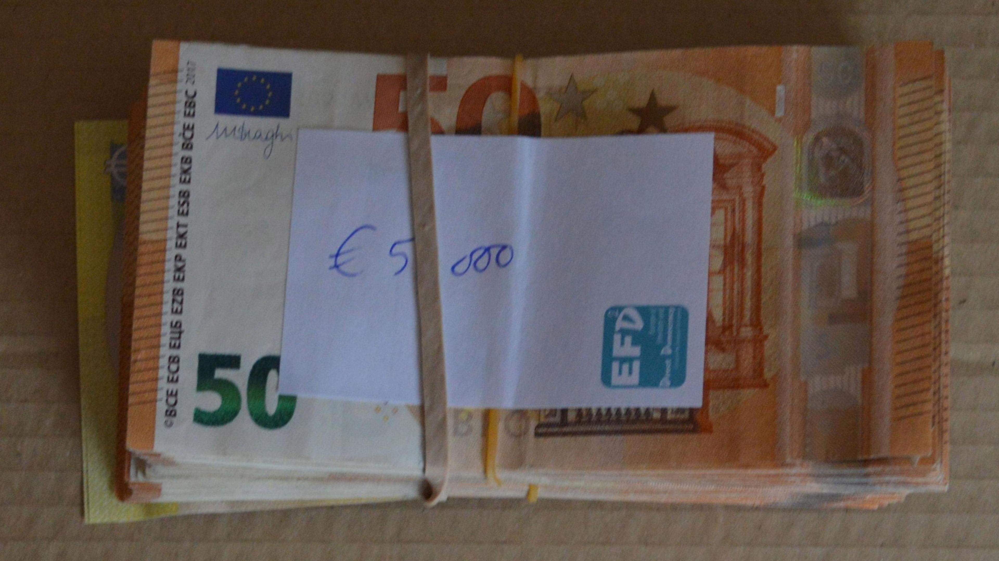 A pile of Euros in notes, grouped by a rubber band with a piece of paper on top which says 5,000 euros.