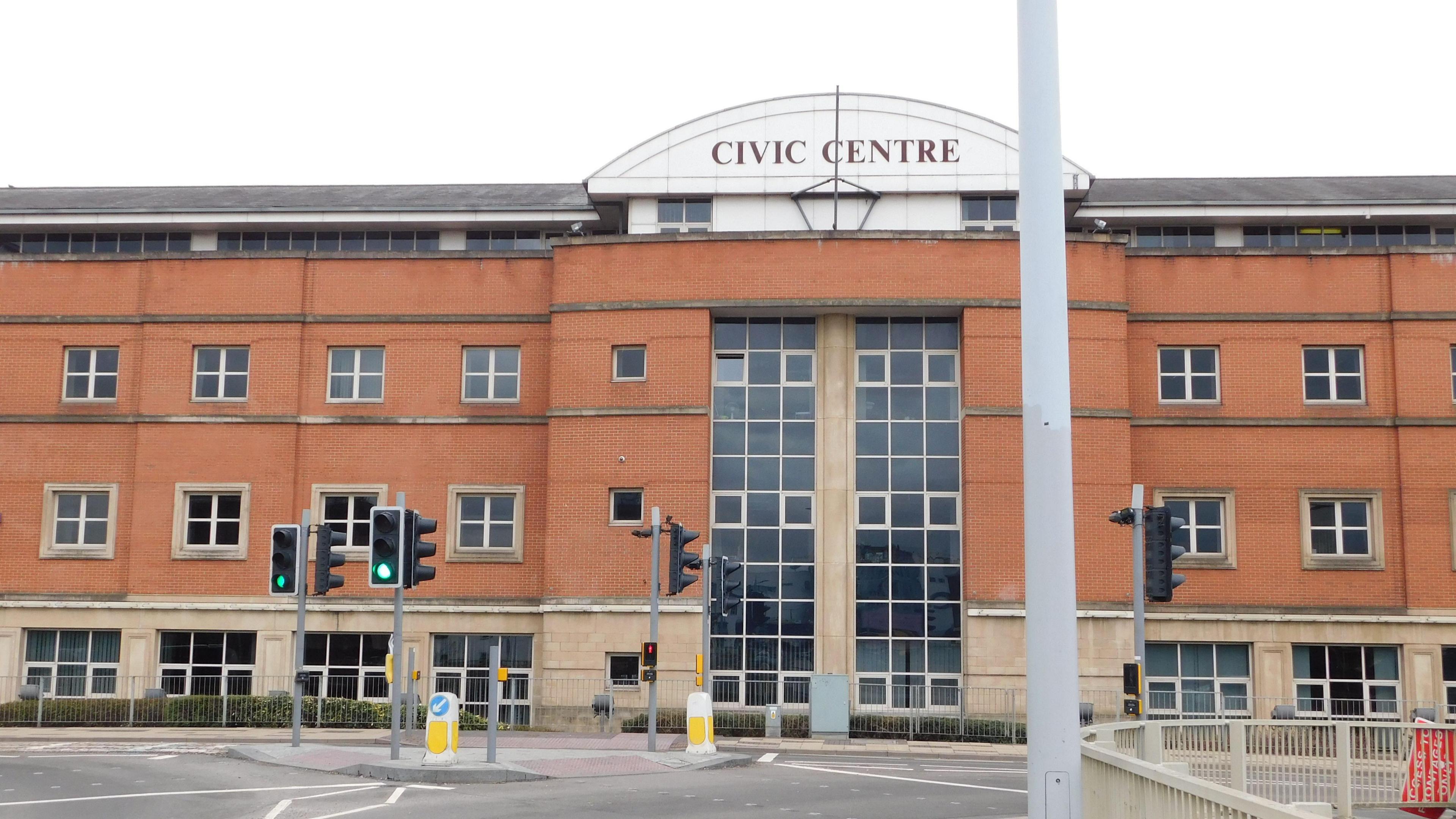 The front building of Stoke on Trent city council's civic centre. It is brown brick with rows of square windows, as well as two vertical strips of windows in the centre. 