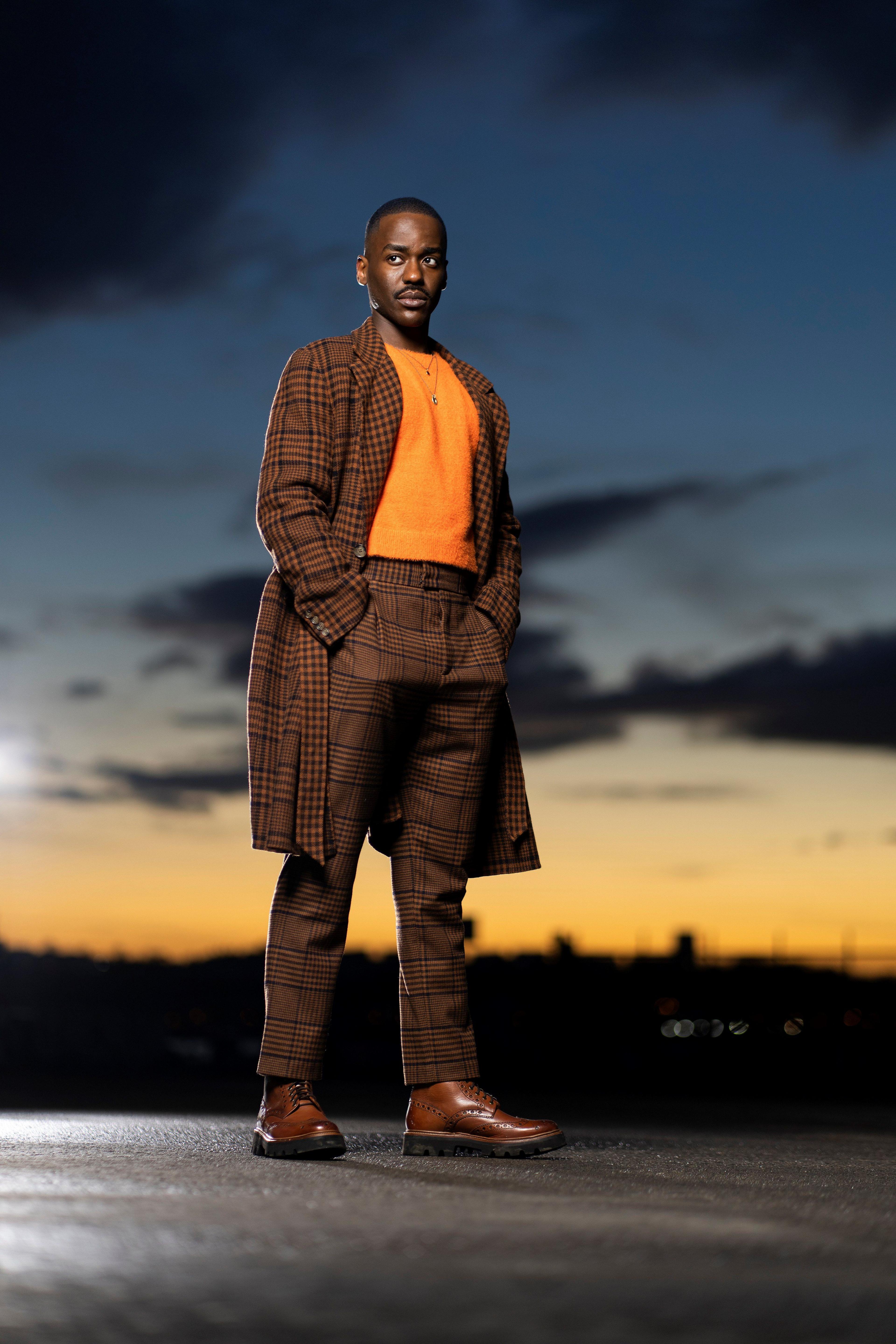 Ncuti Gatwa as The Doctor in a brown suit with an orange jumper