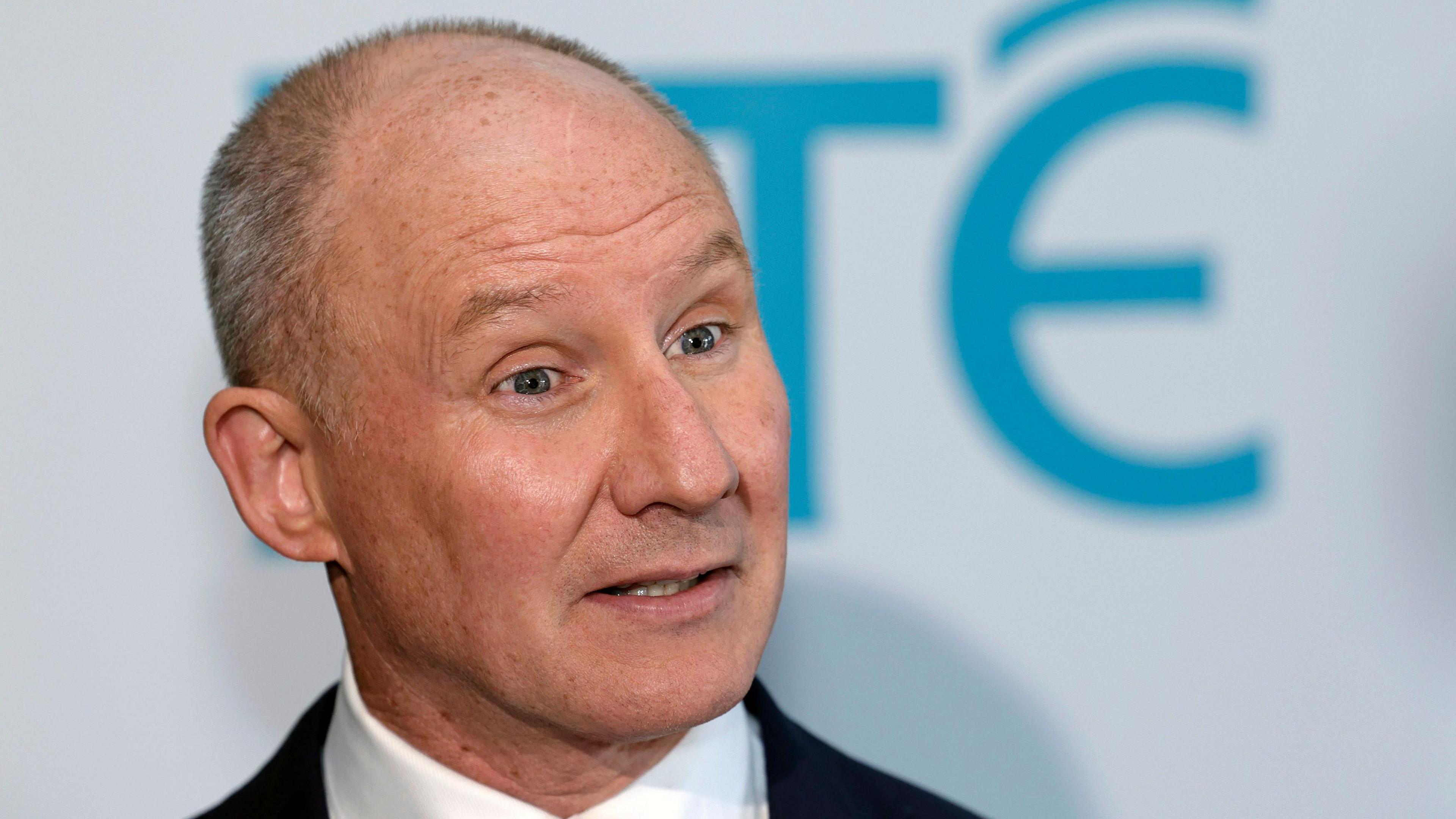 Head and shoulders shot of Jim Gavin. He is a balding man with short, grey hair. He is standing in front of a large board with RTÉ branding