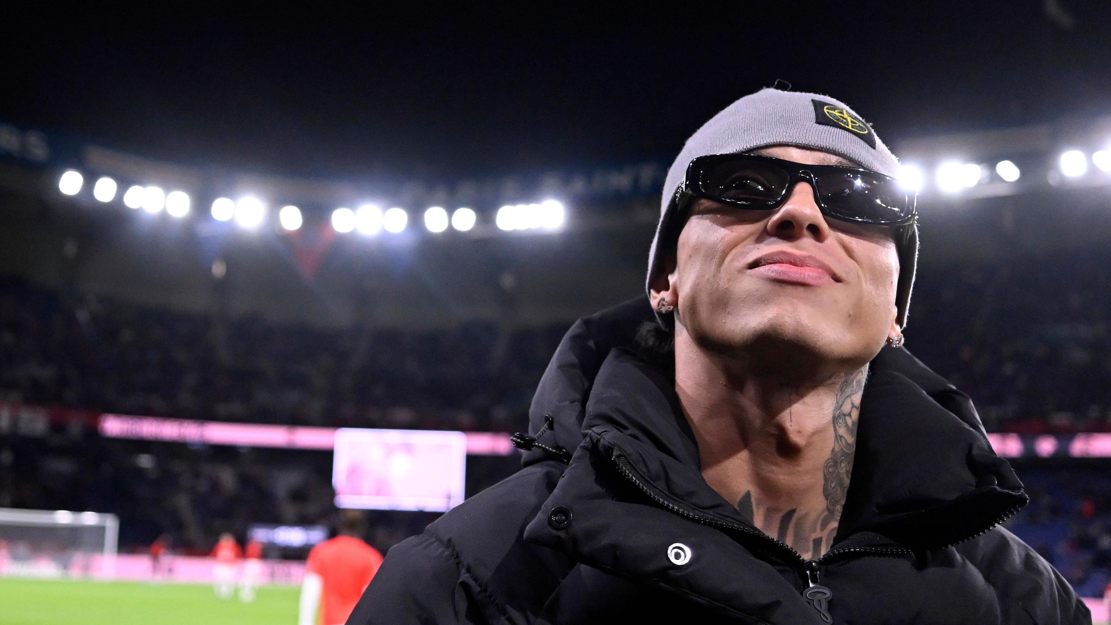 Central Cee, wearing sunglasses, stands on the pitch of Parc Des Princes in France, as he attends a football match in September 2024