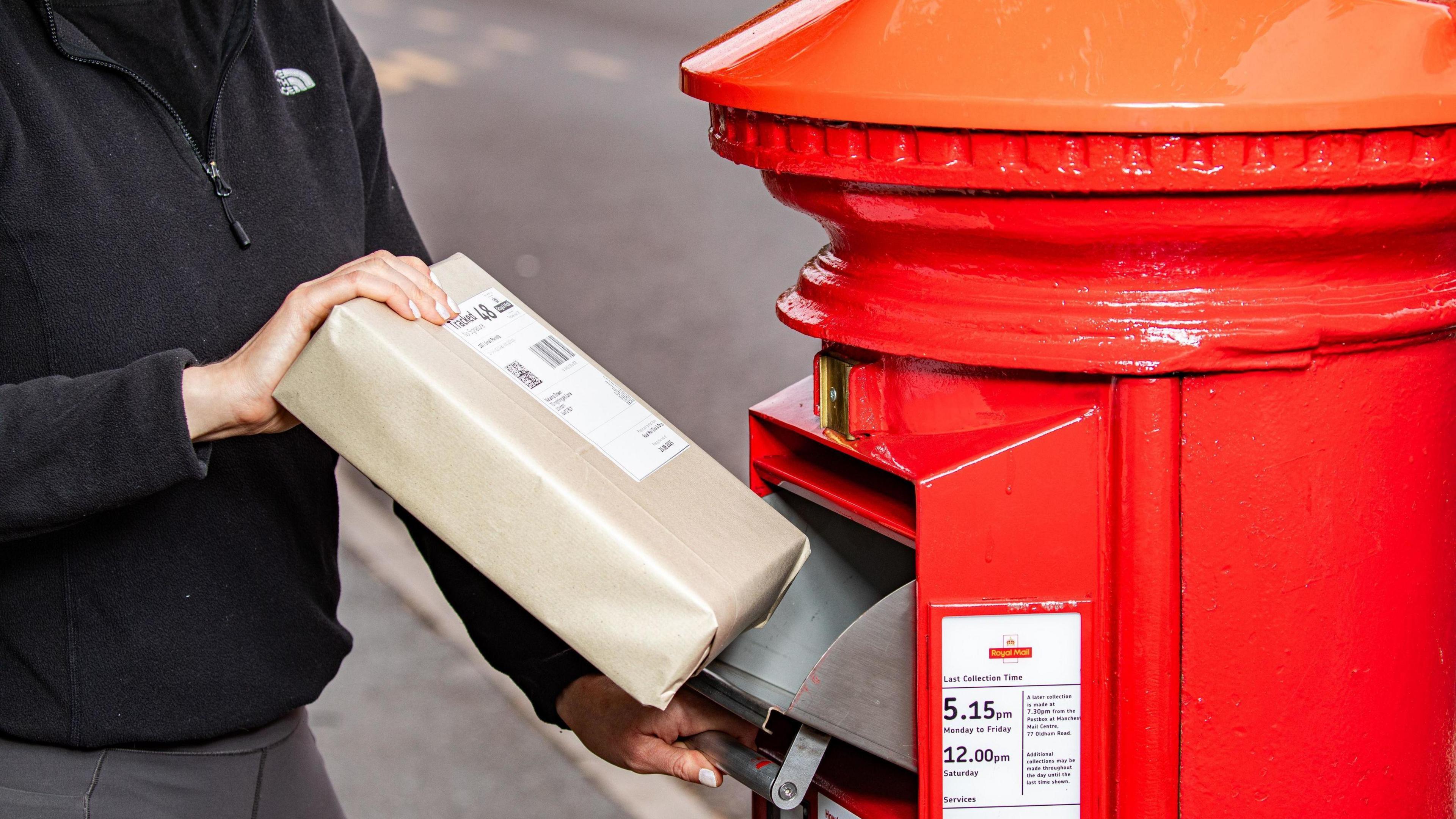 A person is posting a parcel into a red parcel post box