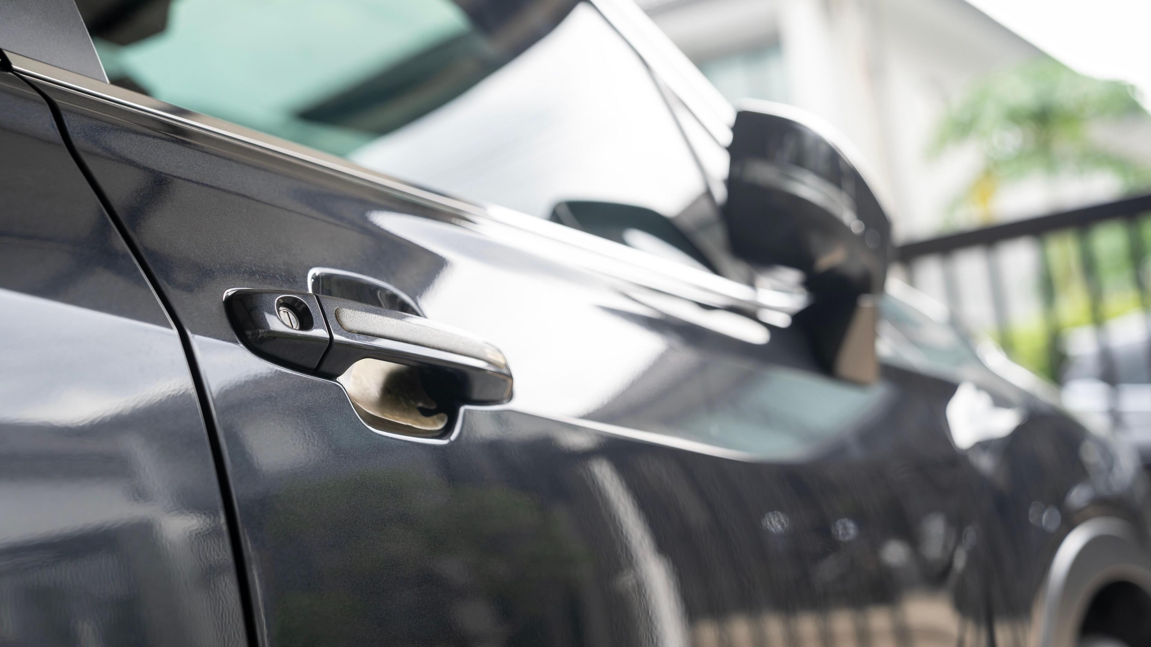 A black car. The door handle and wing mirror can be seen. 