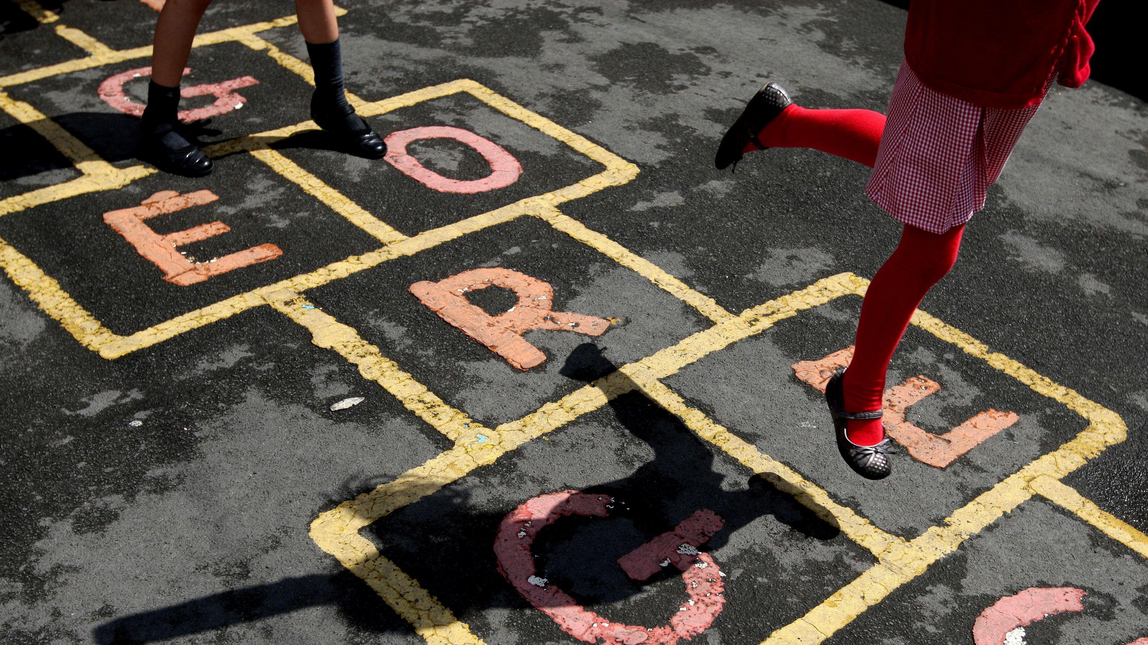 A schoolgirl skips on hopscotch in the playground