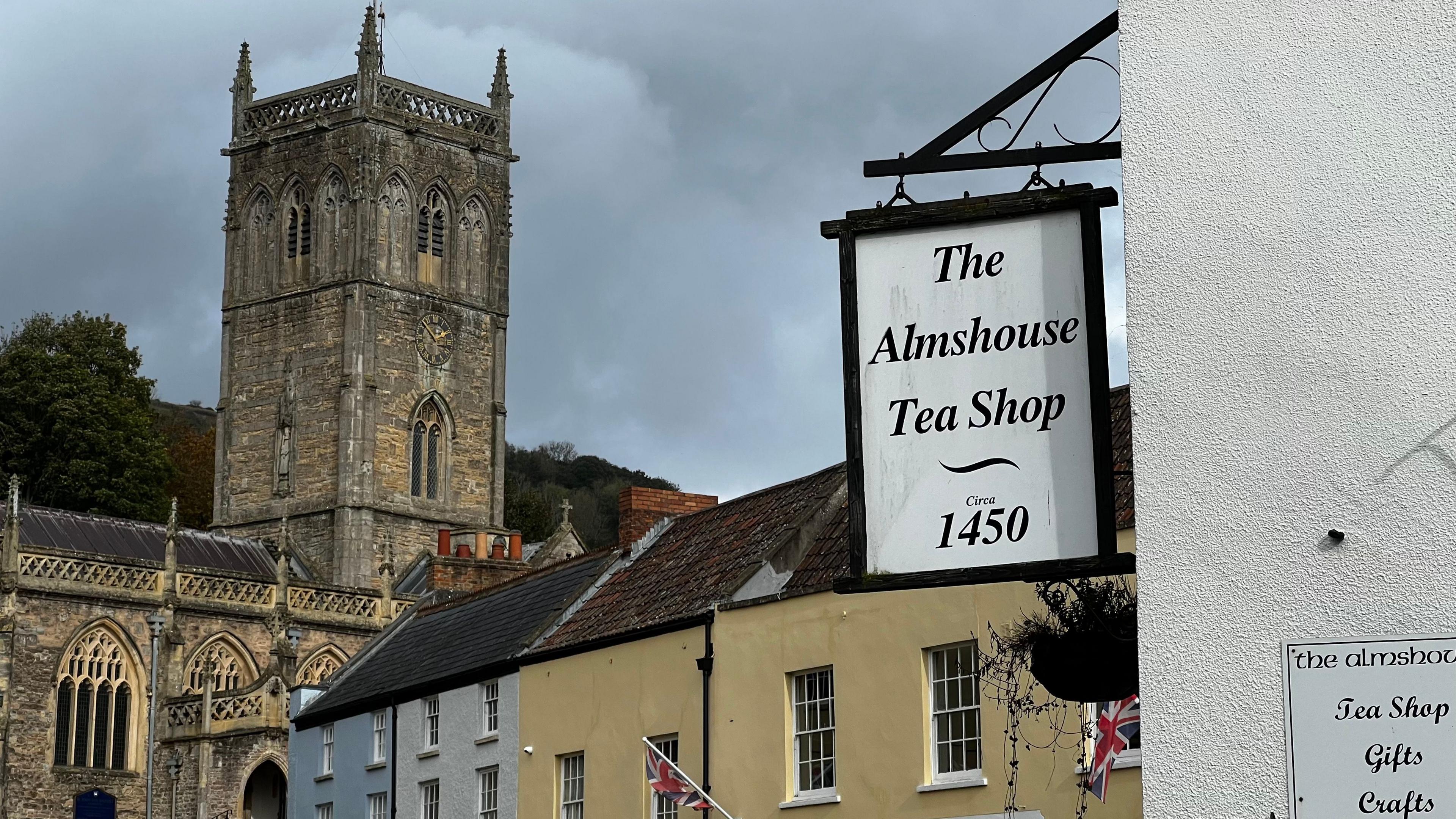 A view over Axbridge town square, towards the old church. In the foreground, a sign reads "The Alms House Tea Shop, established 1450."