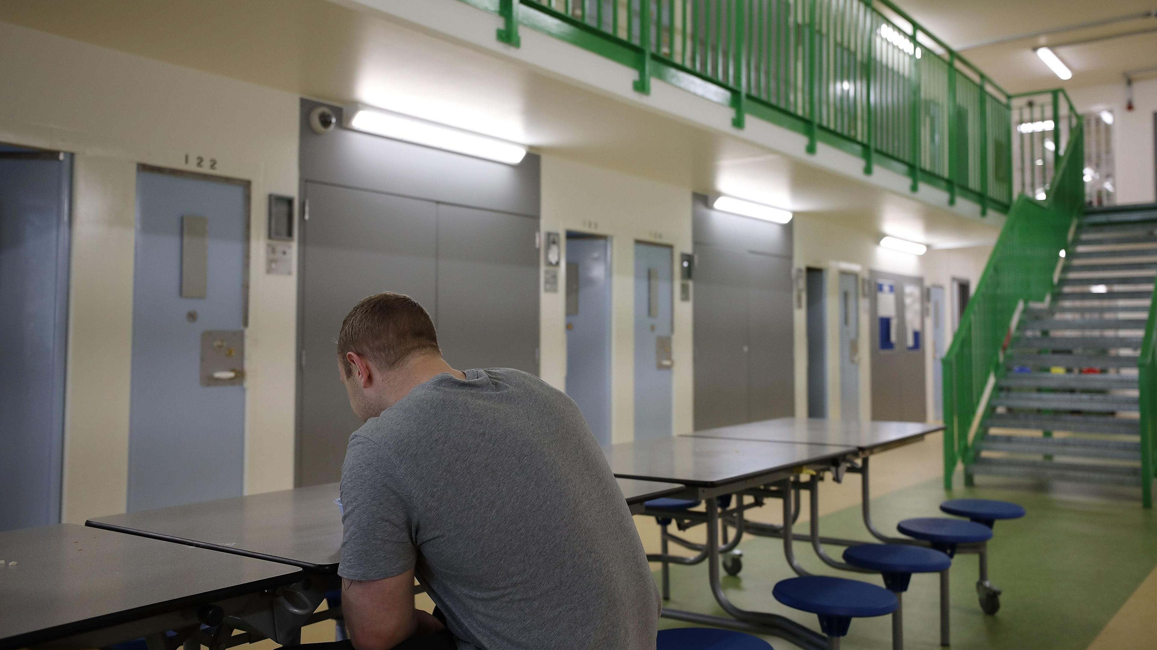 Prisoner sitting at a table in the middle of a prison block on his own