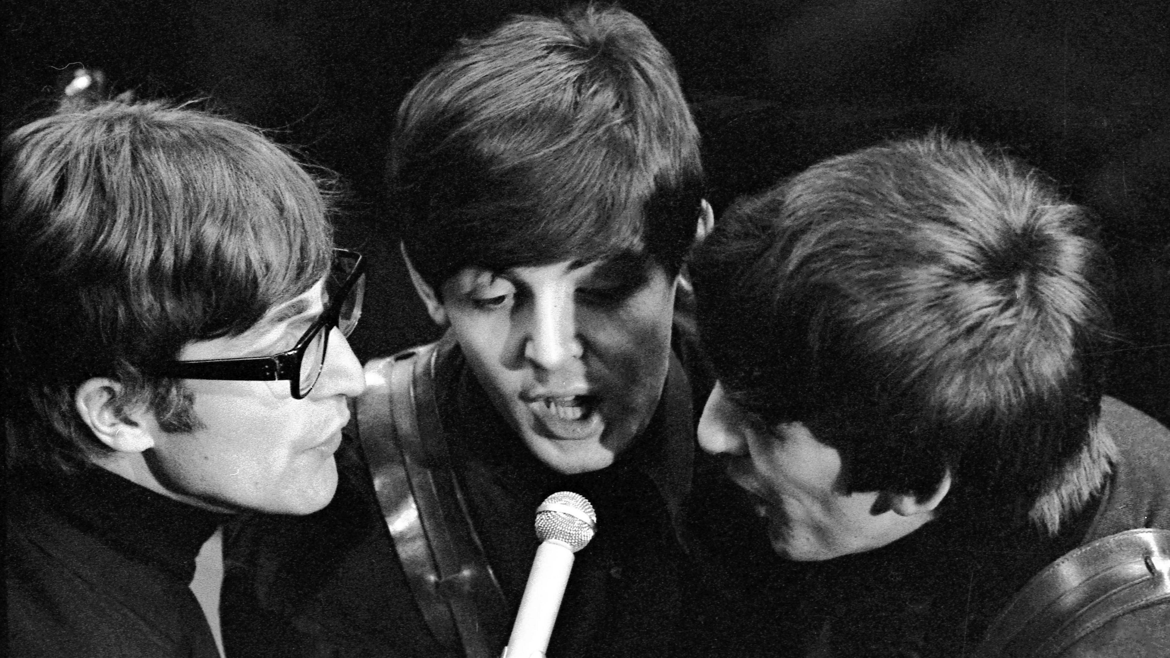 John Lennon, Paul McCartney and George Harrison sing into a microphone