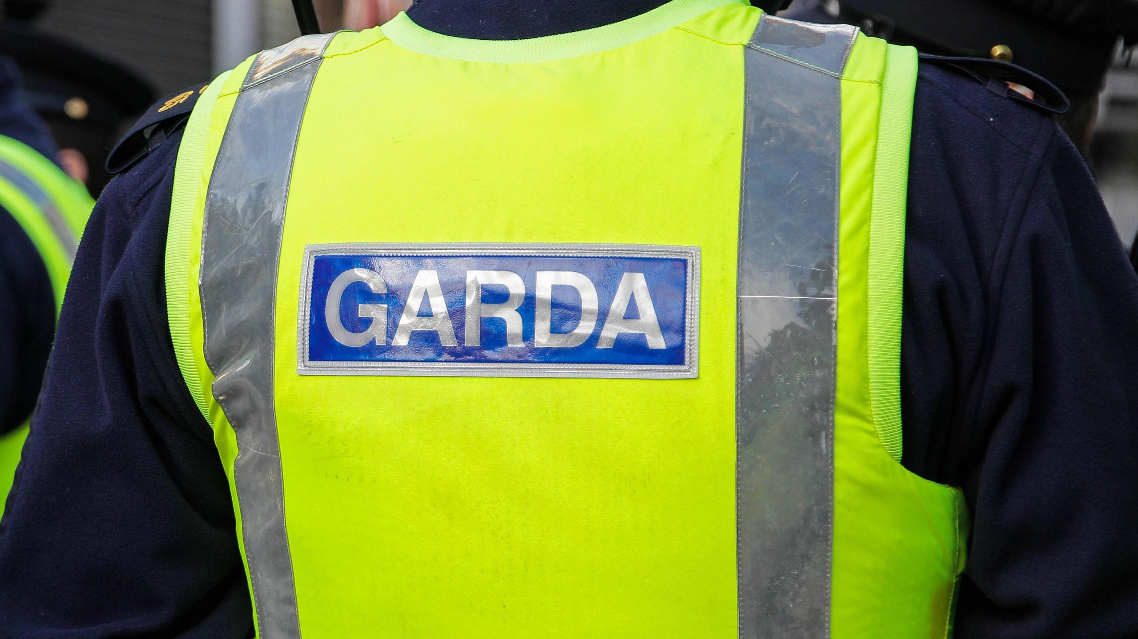 A close-up of the back of a garda officer's uniform. He is wearing a yellow high-viz vest over a navy uniform.