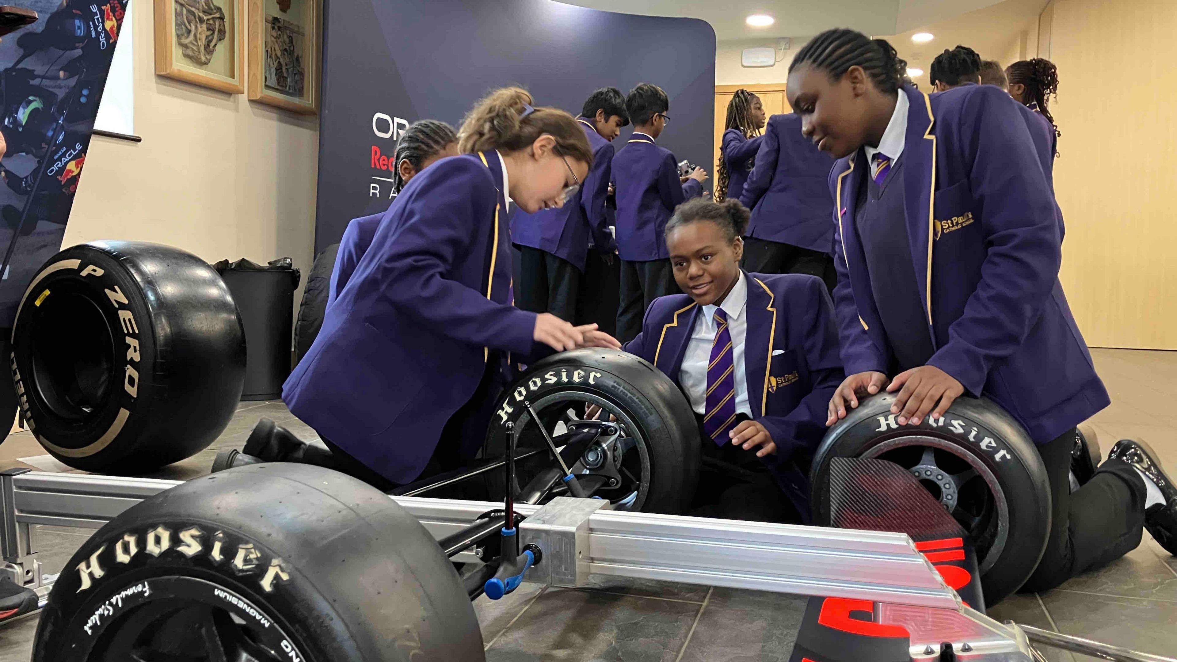 Children in purple school uniform carrying out a mock pit stop on a frame with racing car wheels attached.