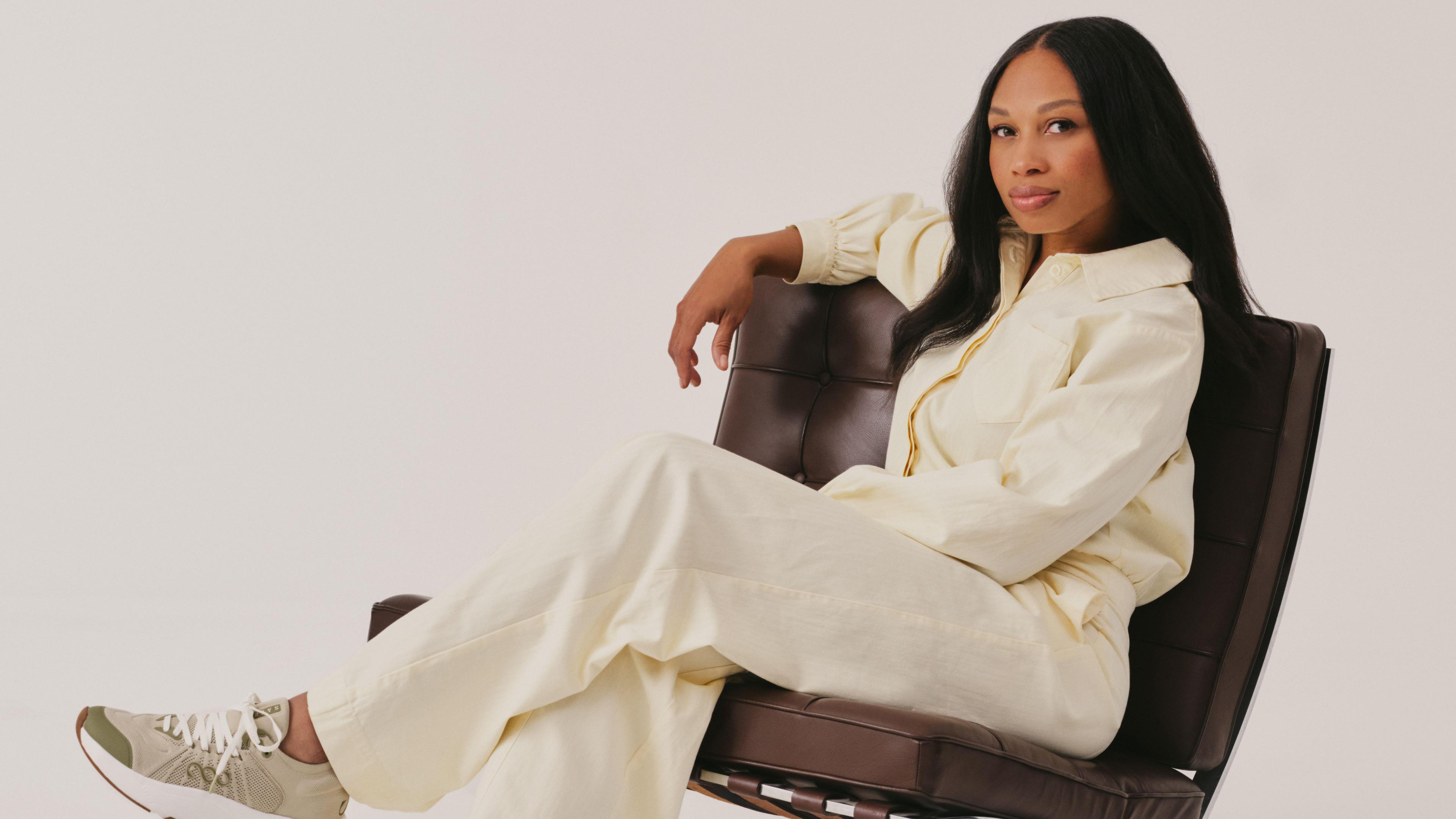 Athlete Allyson Felix sat in a brown leather chair wearing all white and cream trainers.