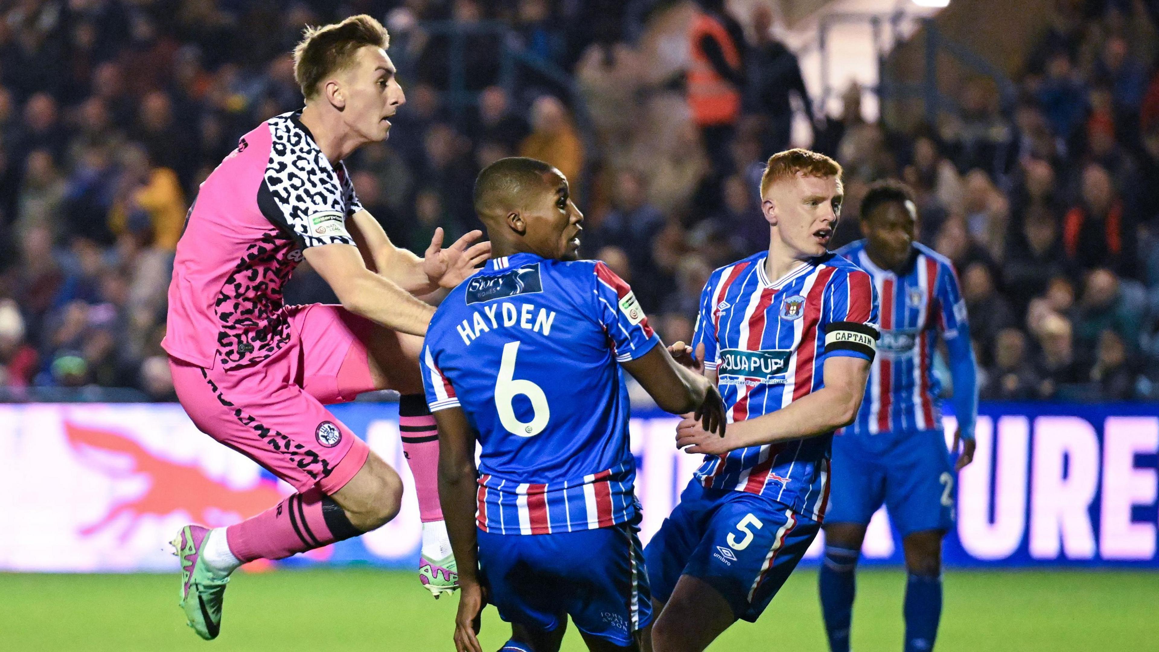 A leaping Harvey Bunker (in pink on left) scores as Carlisle defenders Aaron Hayden (centre) and captain Morgan Feeney watch on 