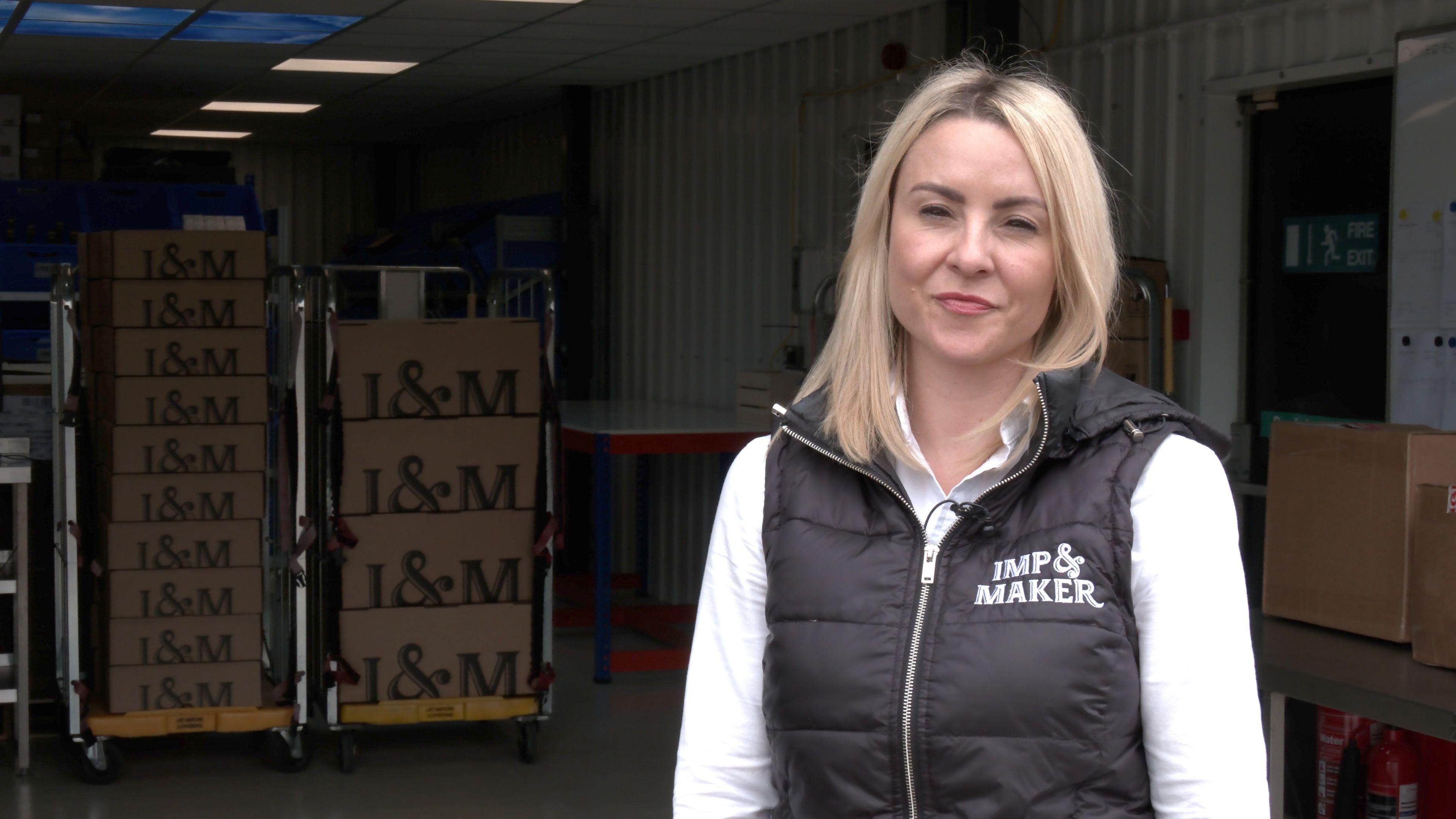 Sarah-Louise Fairburn wearing a black gilet and white long-sleeved top standing in front of a number of pallets with her company's branding on them.