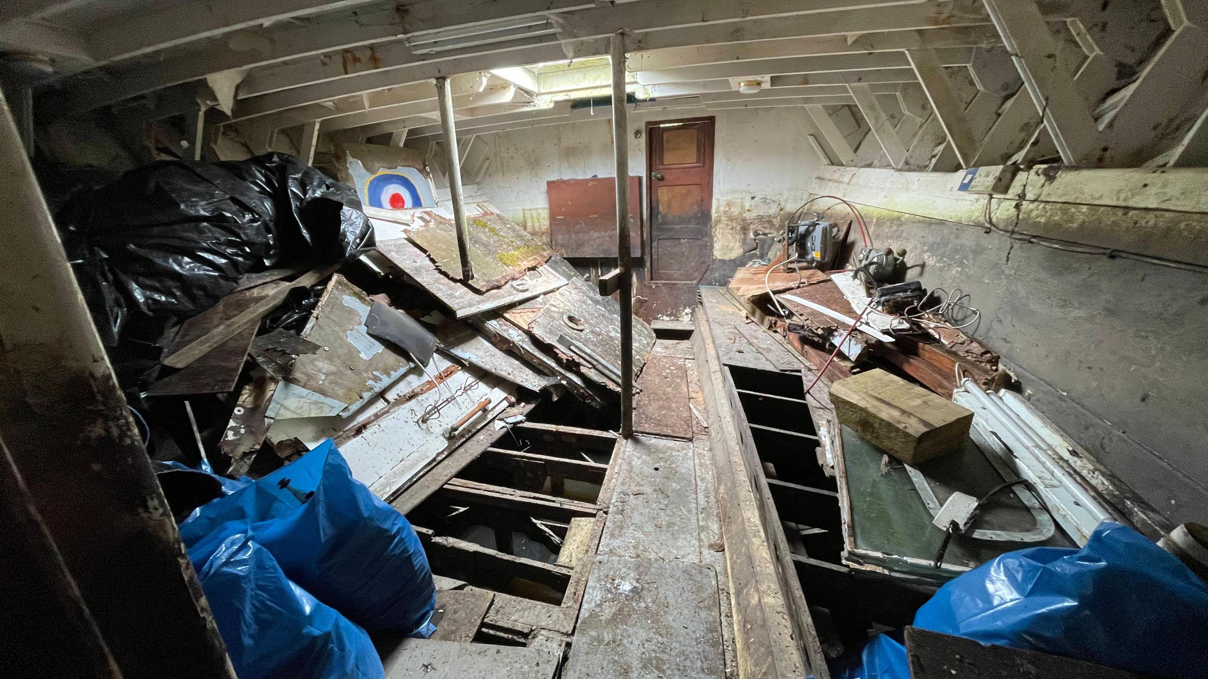 The inside of the whaleback boat shows incomplete wooden flooring and lots of mess