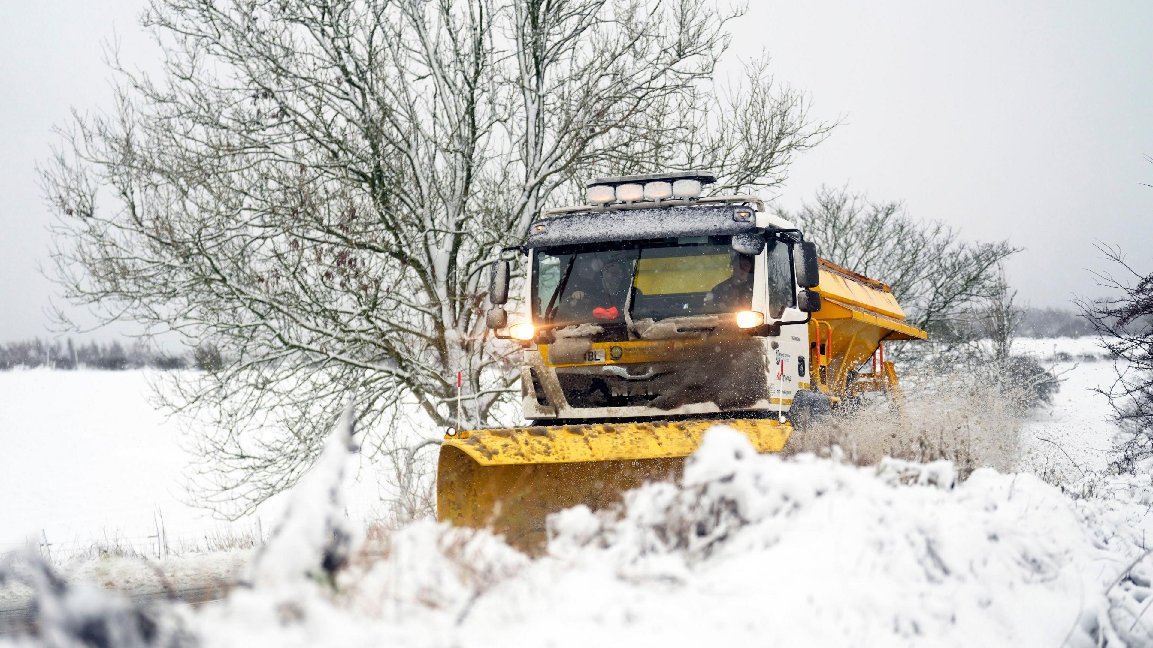 A yellow snow plough goes down a snowy road