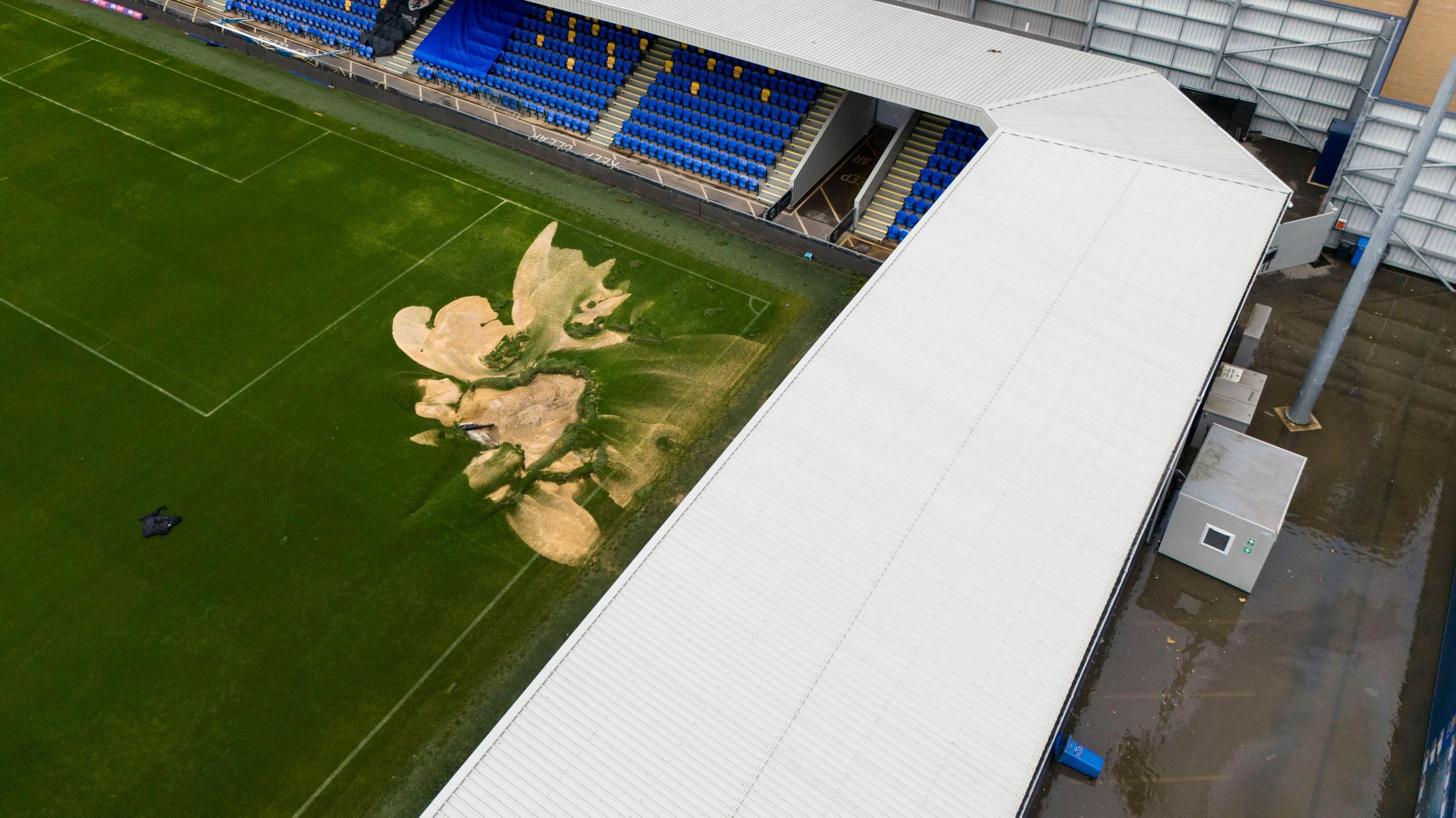 An aerial shot showing sand on the pitch and standing water in the concourse at Cherry Red Records Stadium