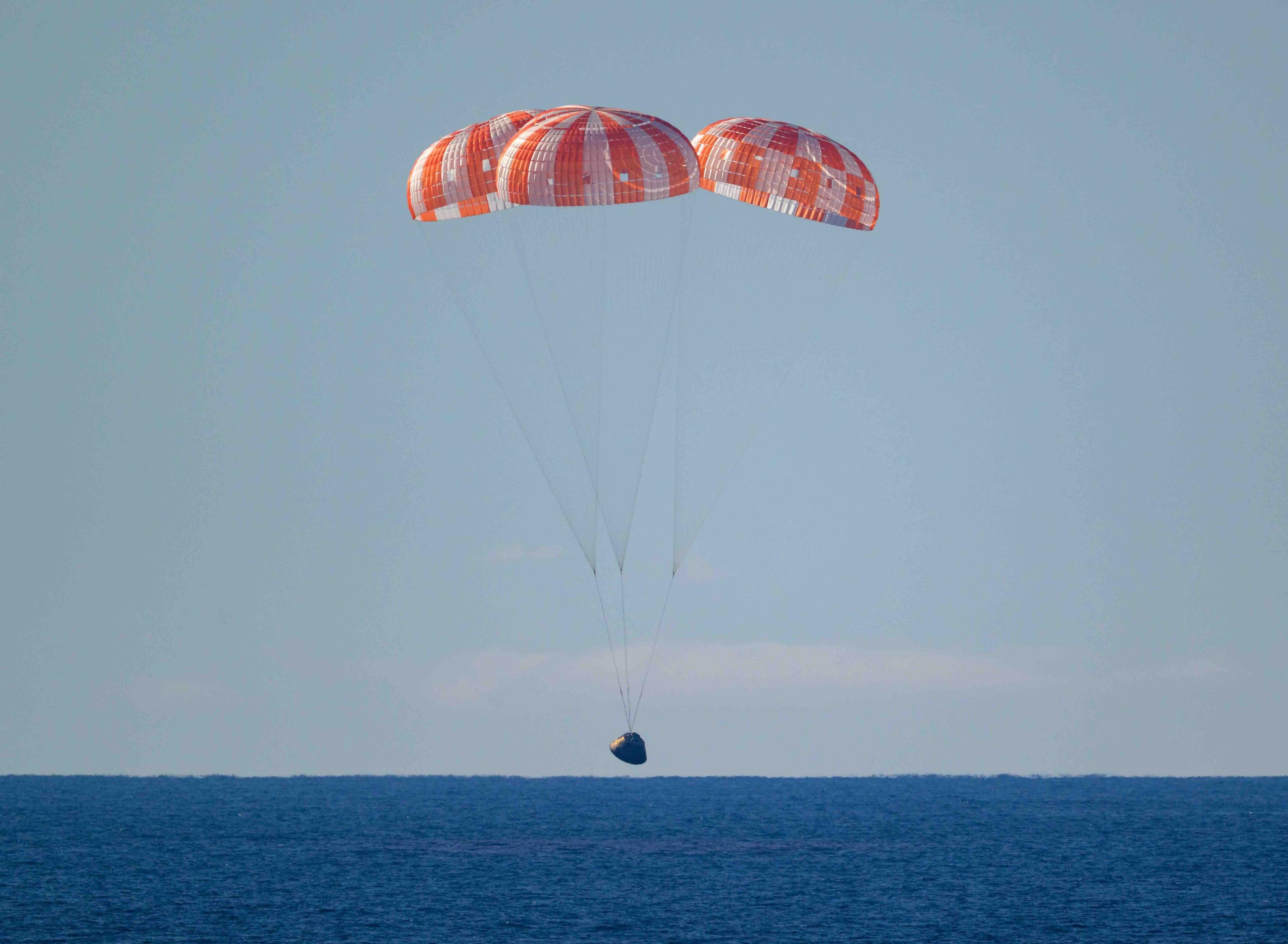The landing craft with it's orange parachutes lands on a dark blue sea.