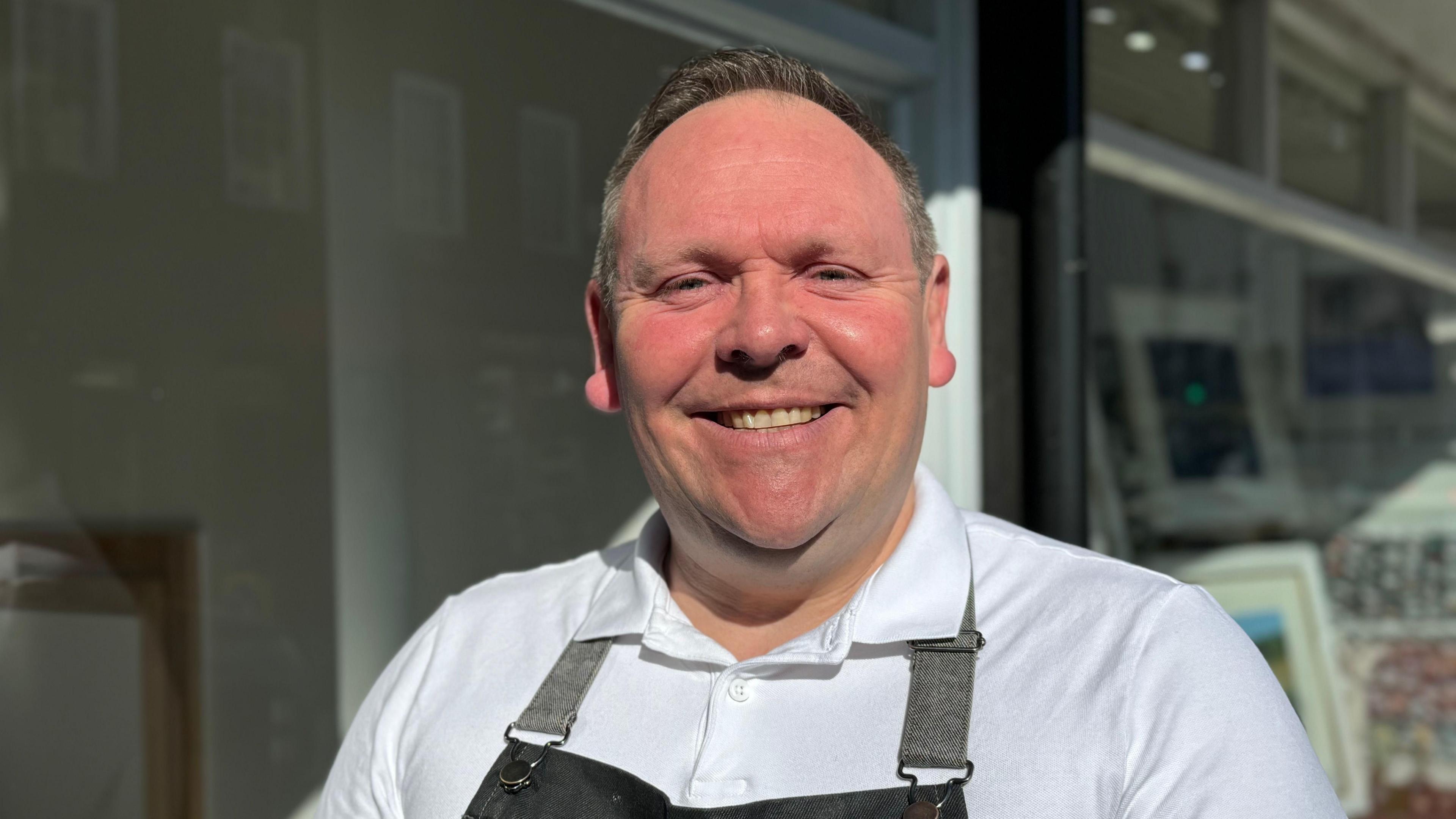 An image of the owner of Hamilton's Tea House, Steve Hamilton. He is looking at the camera and smiling. He is wearing a white top covered by an apron.