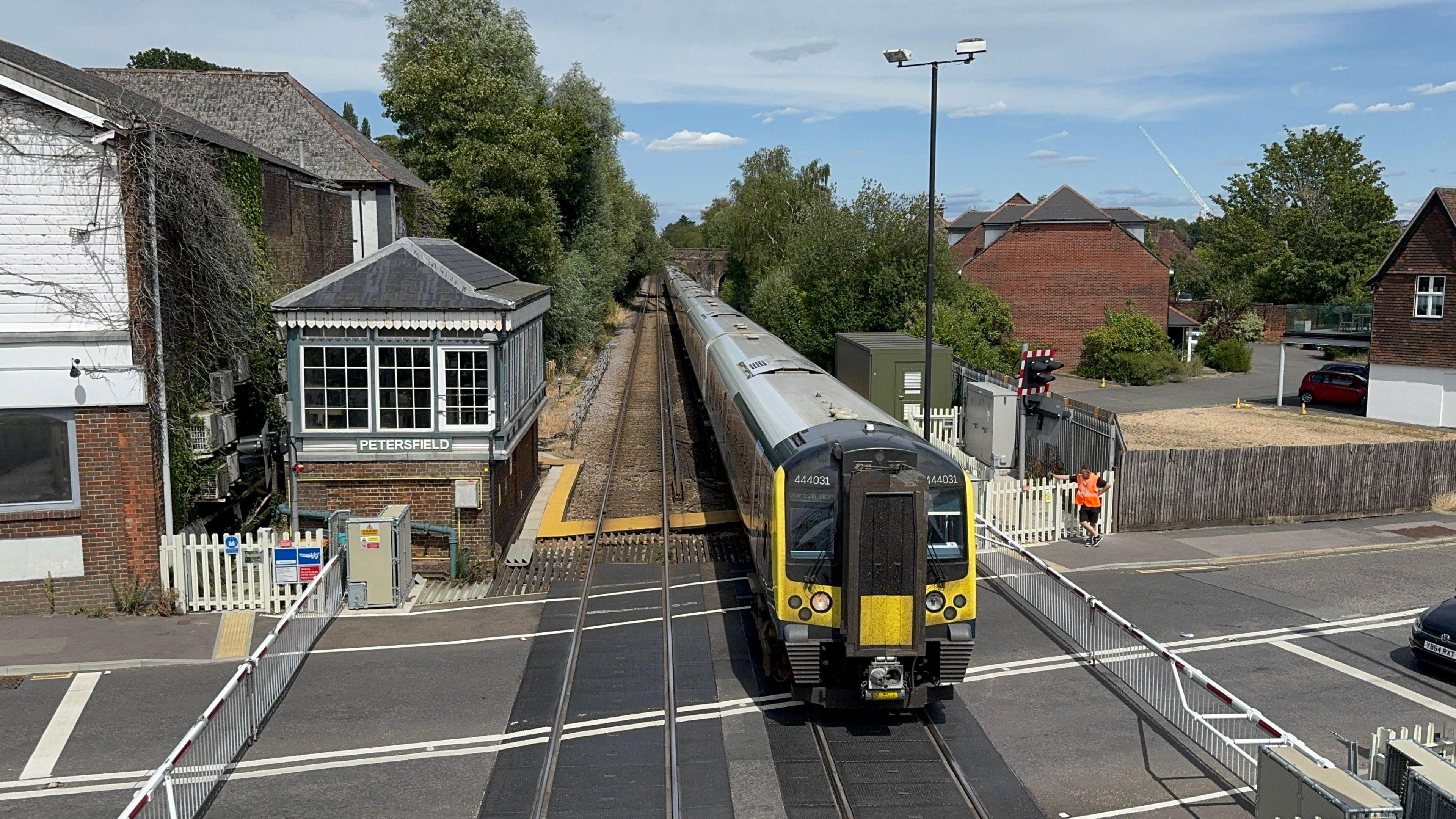 A South Western Railway train crossing a level crossing, where gates are down stopping cars from crossing the road.