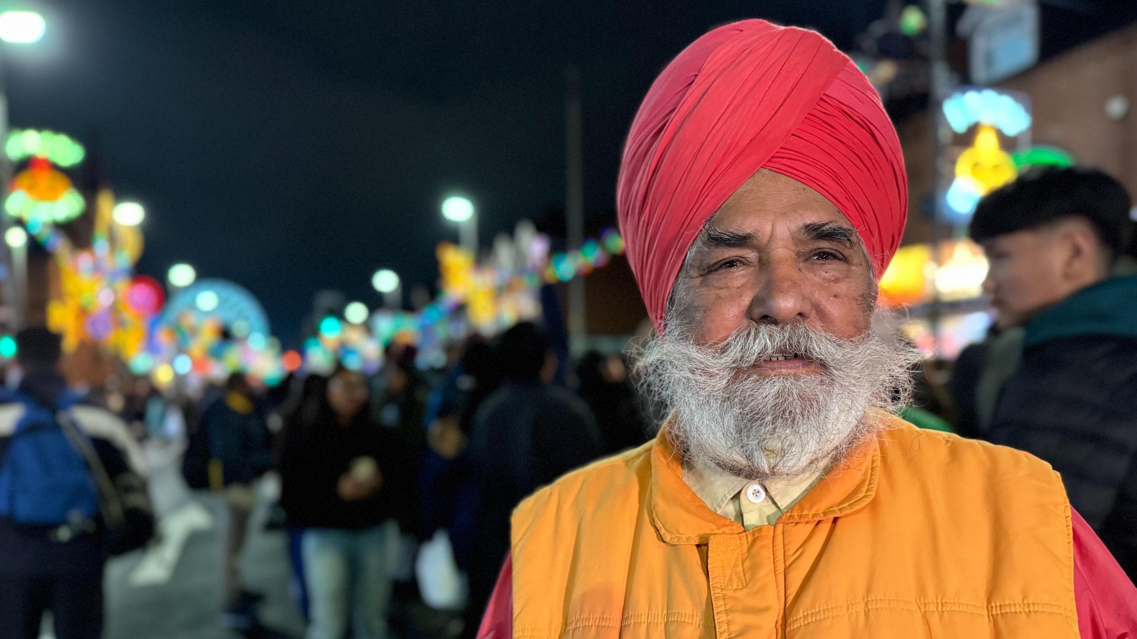 A picture of a man with a beard wearing a turban and orange coat with a yellow buttoned up shirt