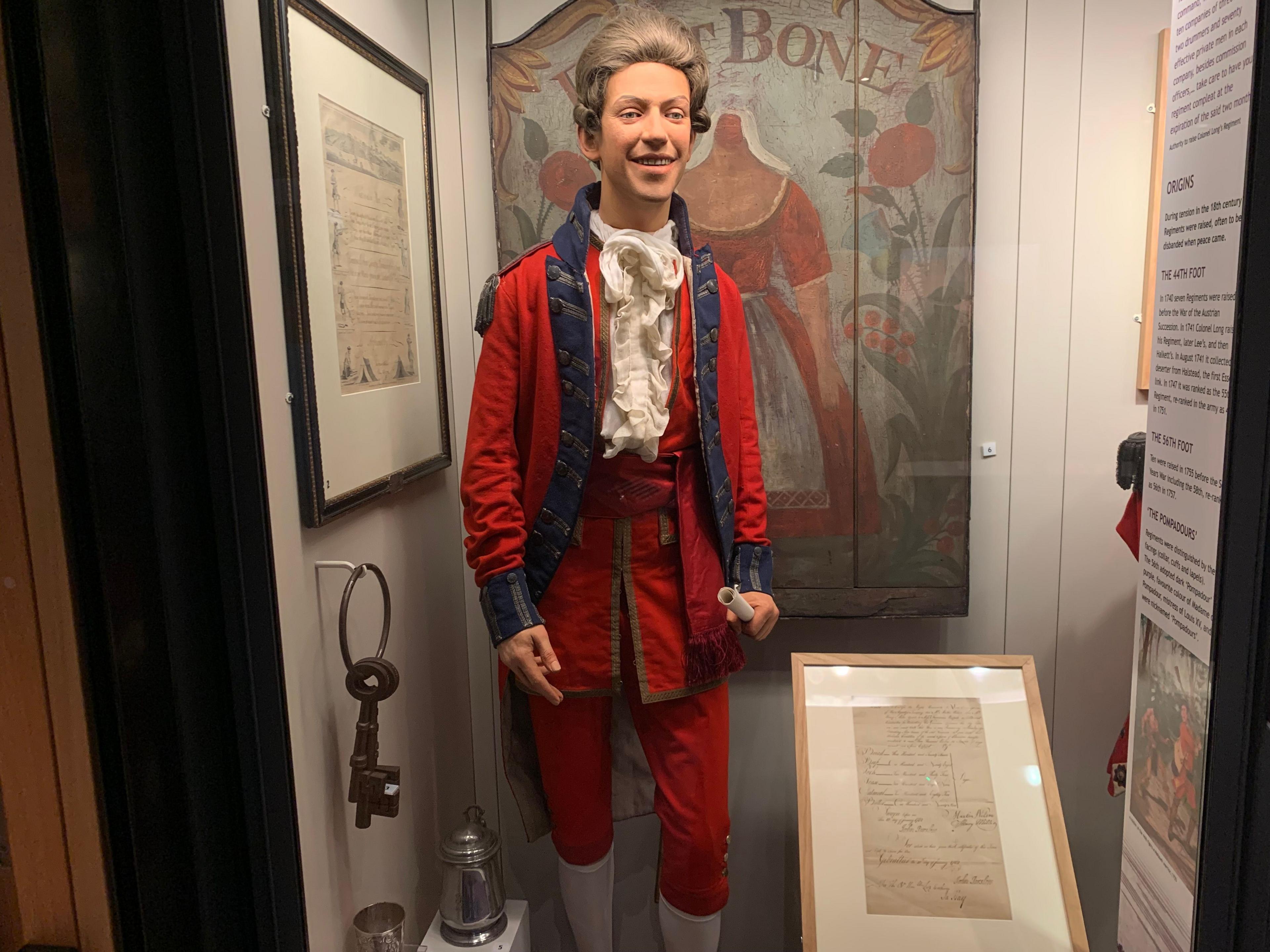 Laurie's model is dressed in a field officer's coatee of the 56th Regiment of Foot dating from 1782. It is red with blue lapels, and he is wearing a white necktie. He is wearing a grey wig, typical of the Georgian era.