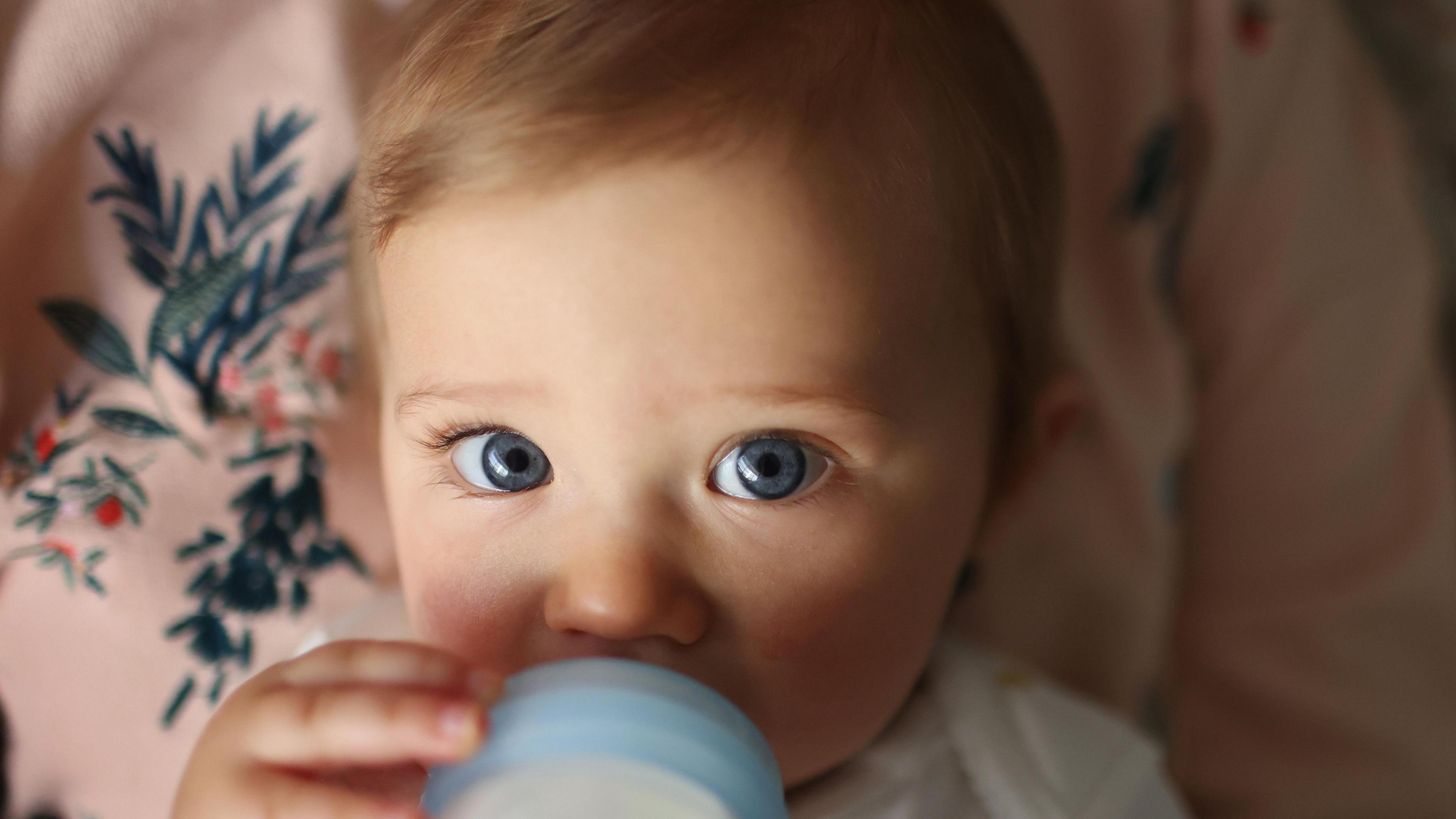 Baby with fair hair and blue eyes drinking bottled milk