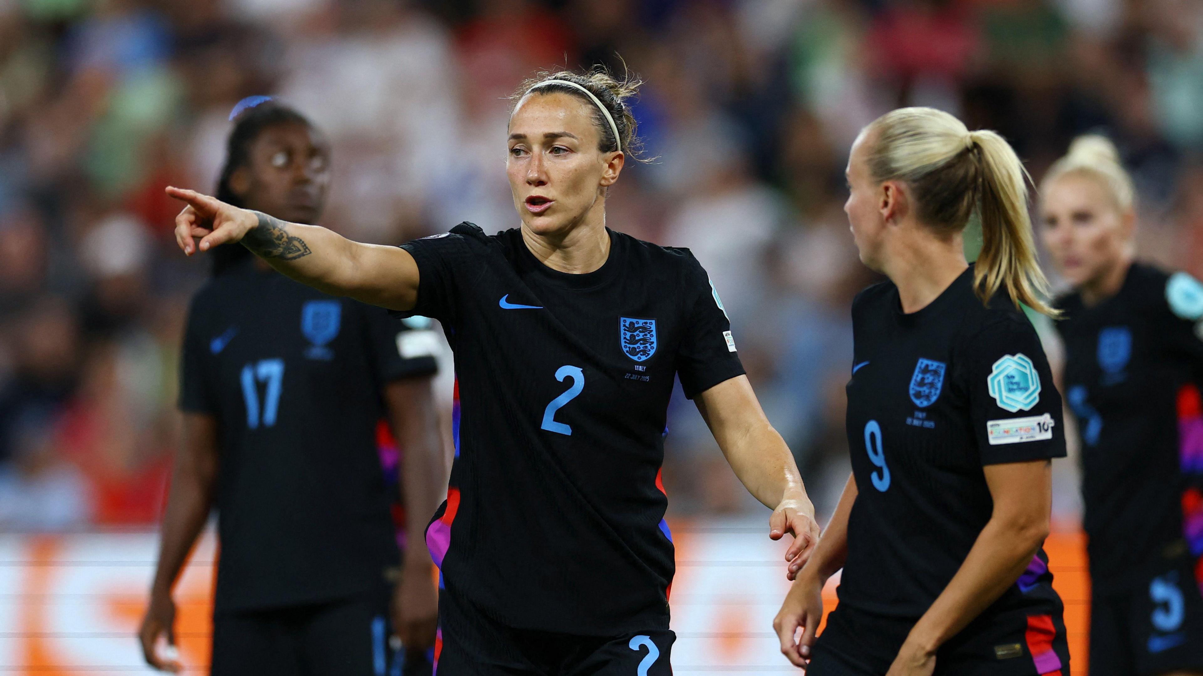 Lucy Bronze speaking to her teammates during the UEFA Women's Euro 2025 semi-final against Italy. Lucy is pointing to something out of shot while her teammates look to her. They are all wearing England's black away kit.