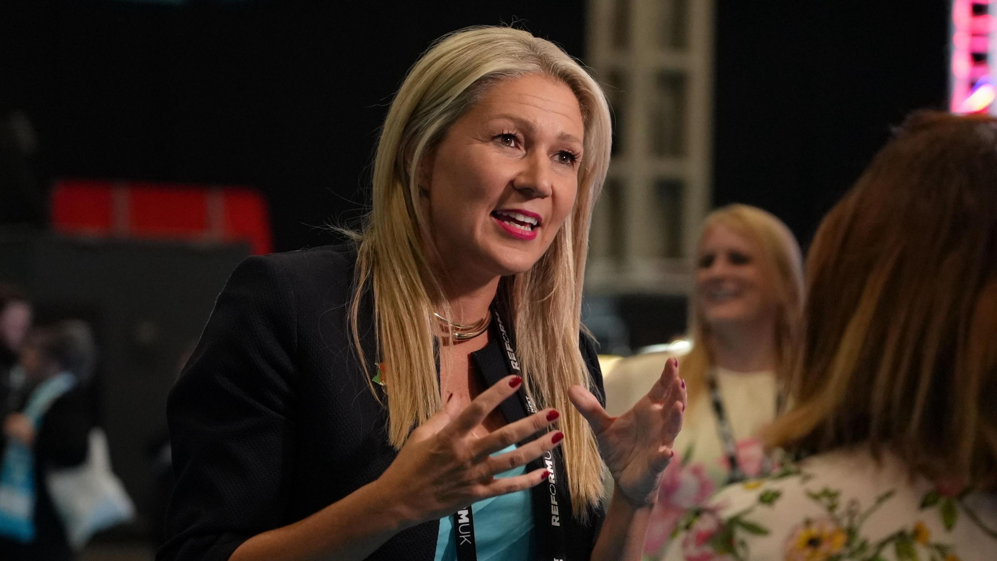 Laura Anne Jones stood on the centre of the photograph talking to a woman stood to the right of her. Jones is wearing a black jacket and a teal top.
