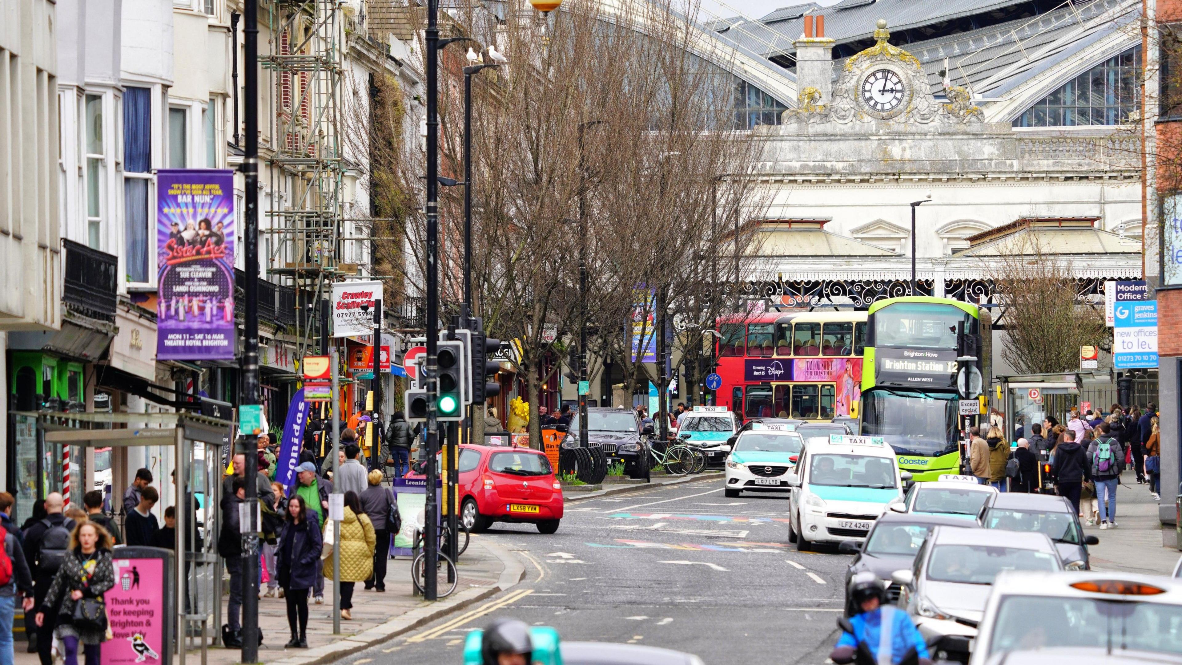 A view up Queen's Road in Brighton, towards the main railway station, with cars, buses and pedestrians filling the roads and pavements.